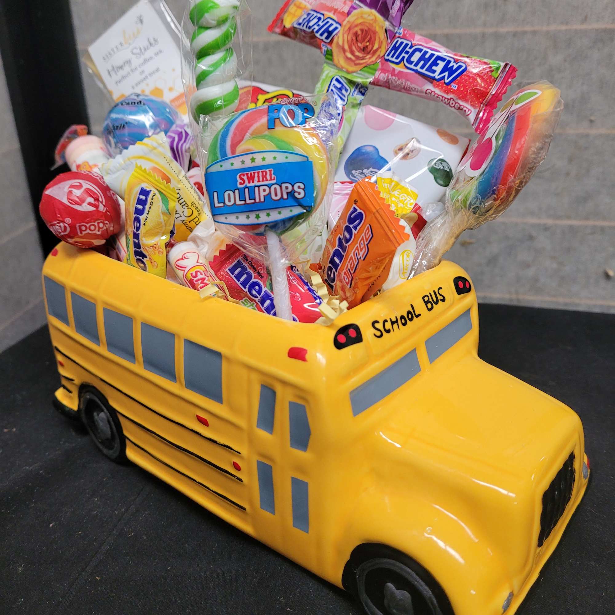 Yellow school bus-shaped candy container filled with assorted lollipops and sweets