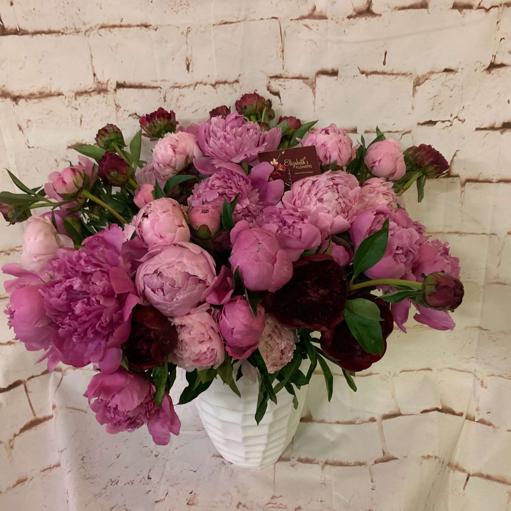 Large arrangement of pink and burgundy peonies in a white textured vase