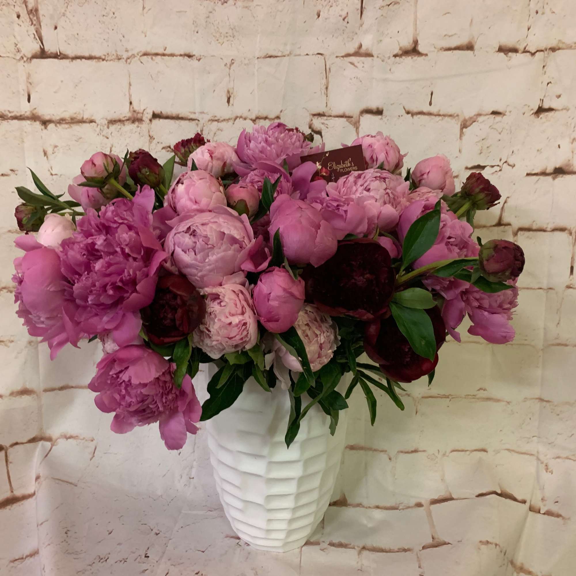 Rounded arrangement of pink and burgundy peonies in a textured white vase