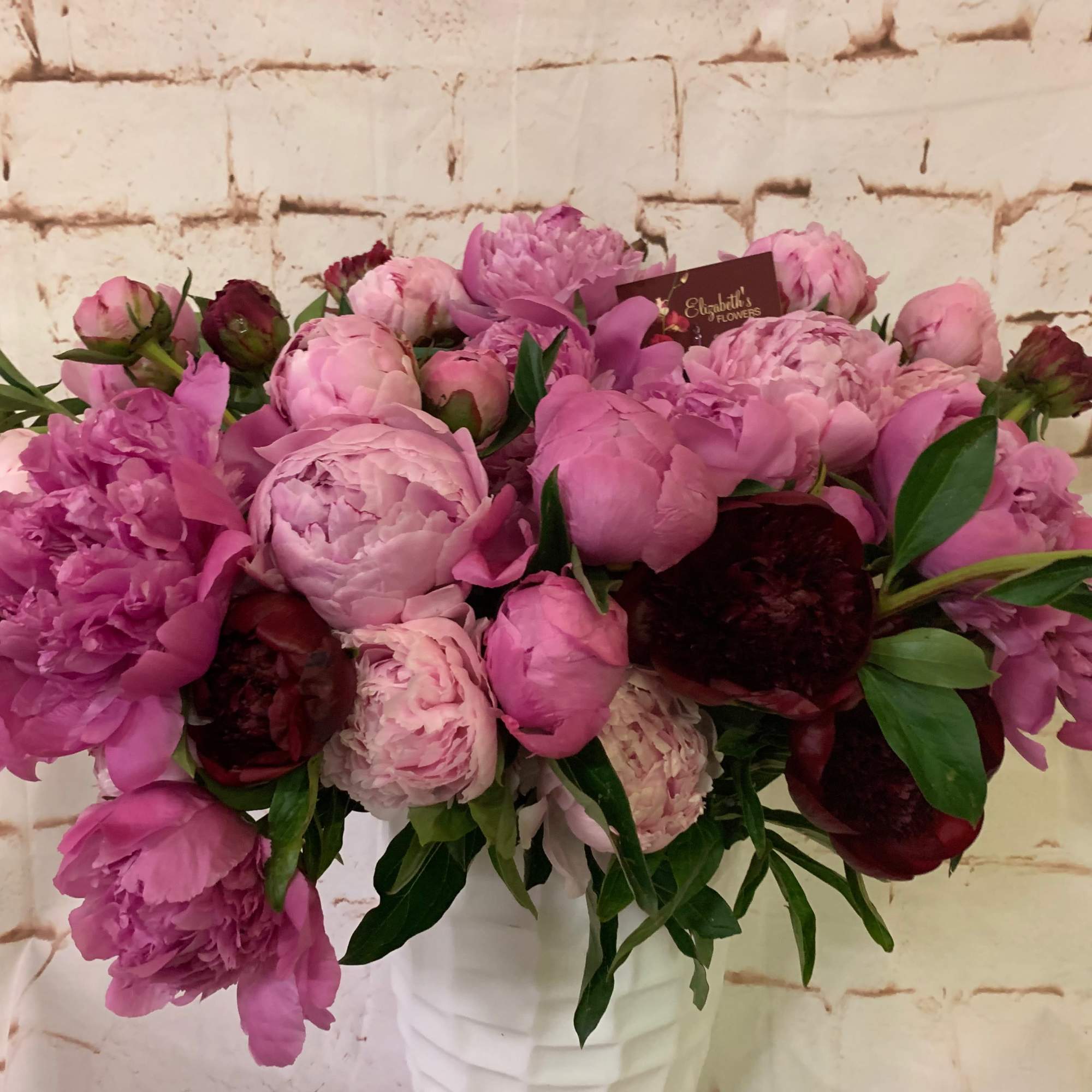 Lush arrangement of pink and burgundy peonies in a white textured vase