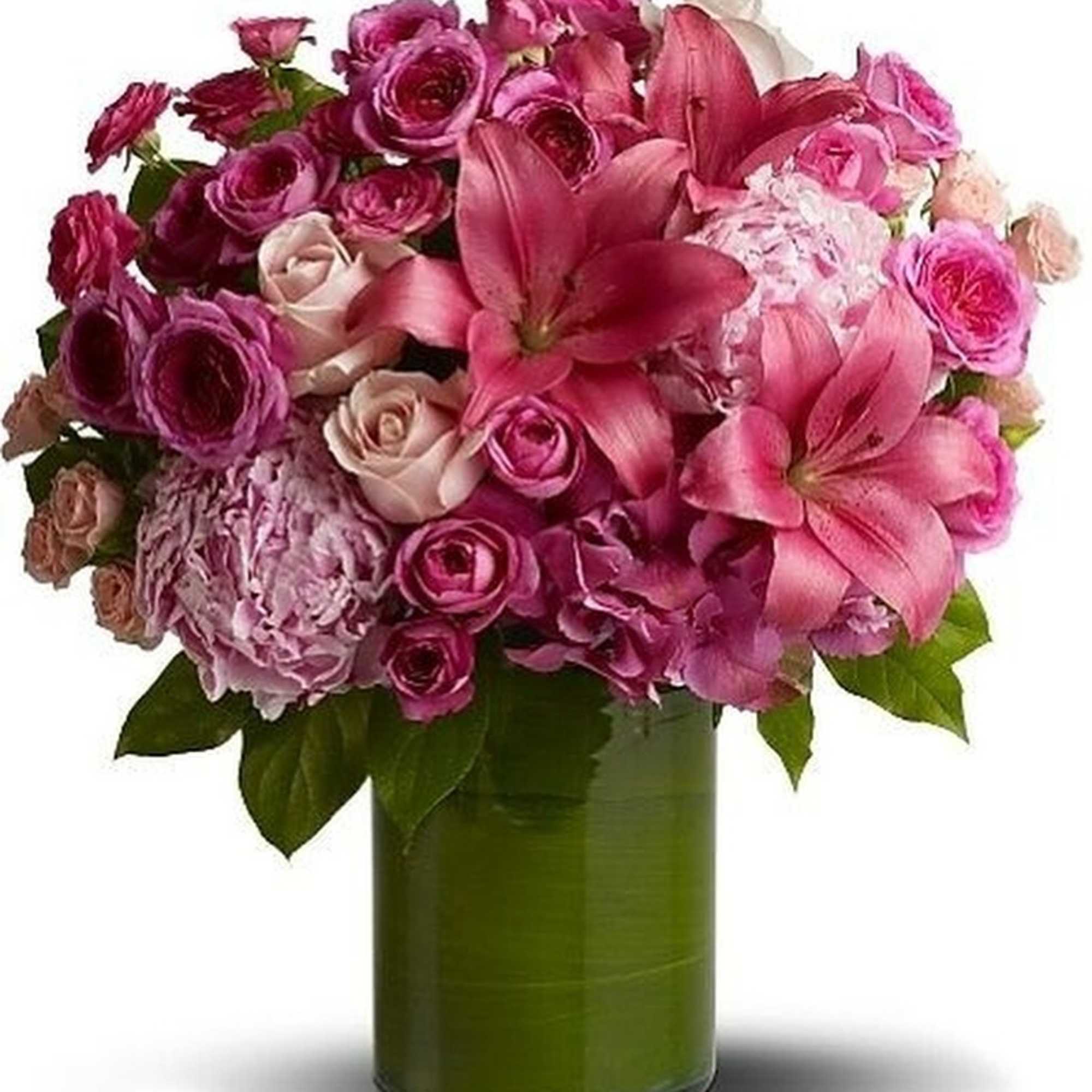Pink lilies, roses, and hydrangeas arranged in a round bouquet in a green-lined glass cylinder vase
