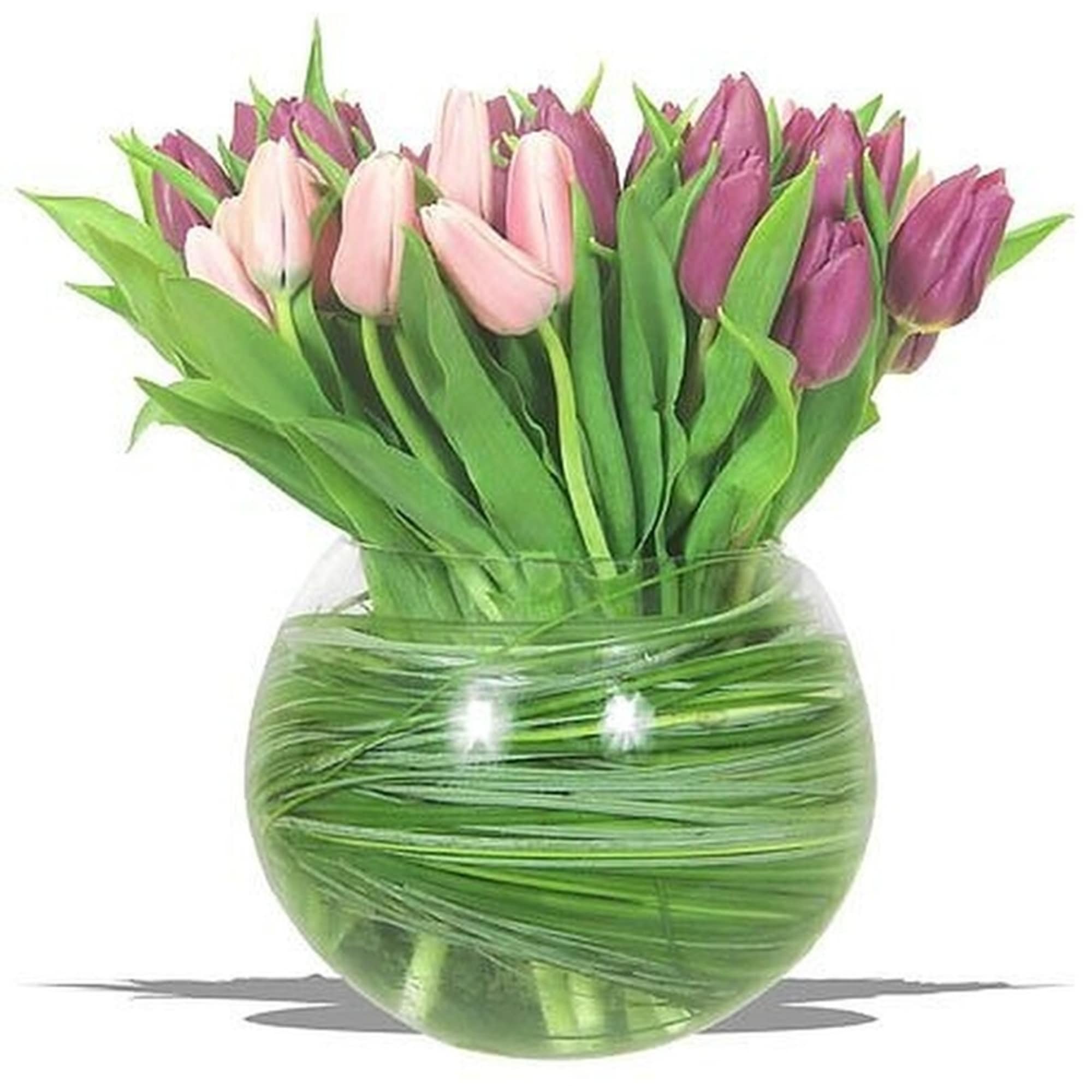 Pink and purple tulips arranged in a round clear glass bowl vase wrapped with green foliage