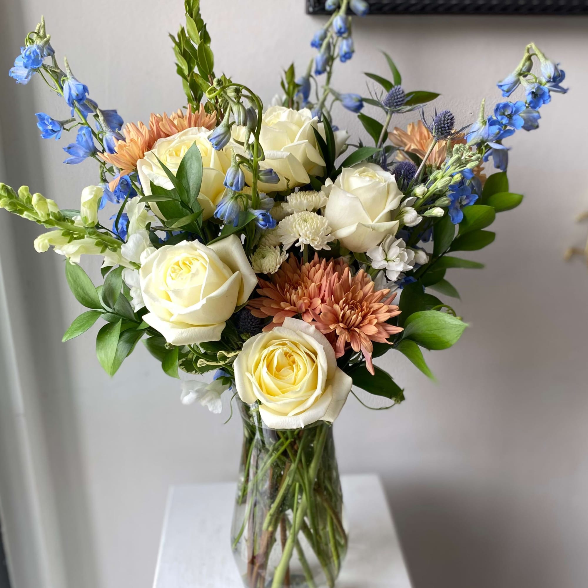 Bouquet of cream roses, blue flowers, and peach blooms in a clear glass vase