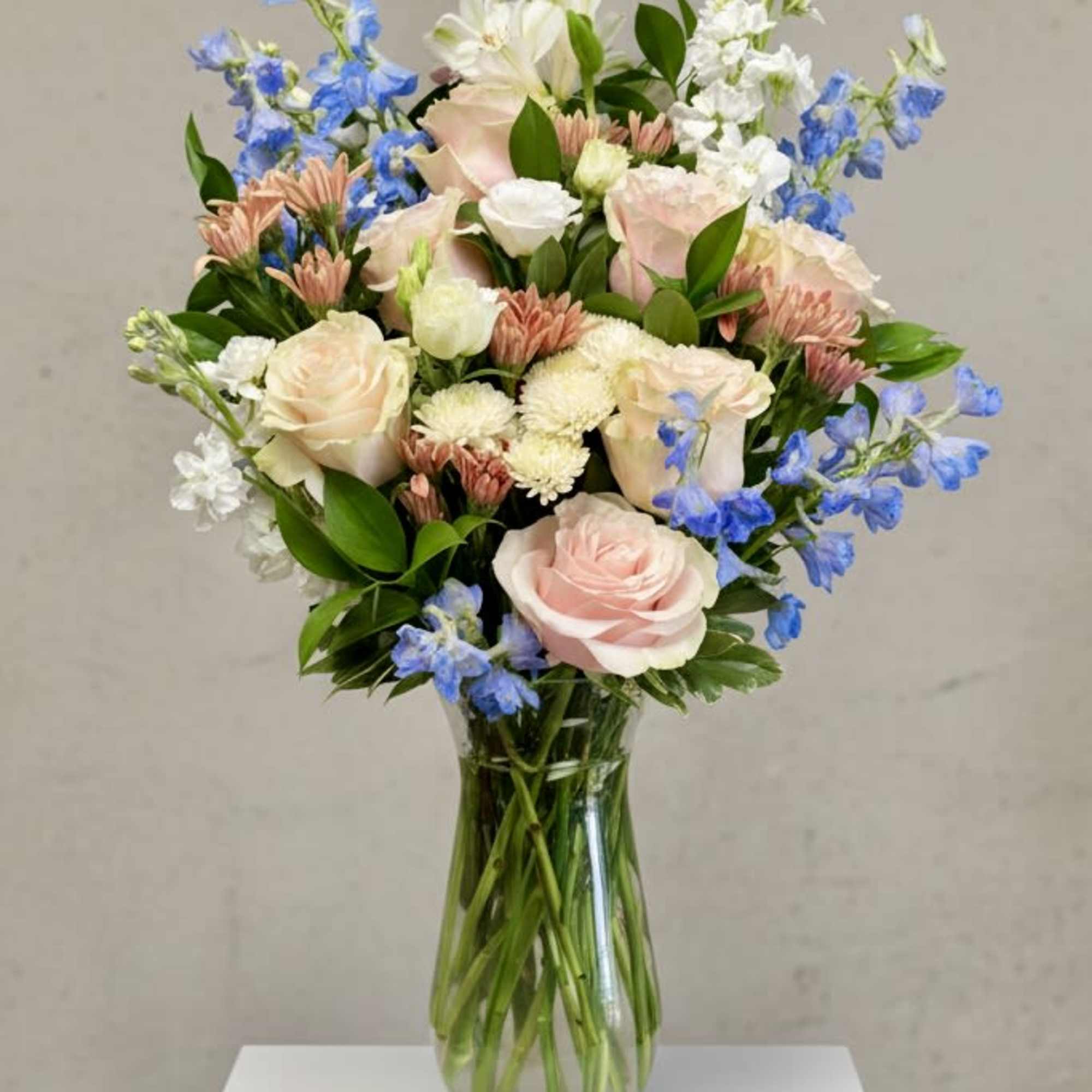 Pastel bouquet of roses, white blooms, and blue flowers in a glass vase