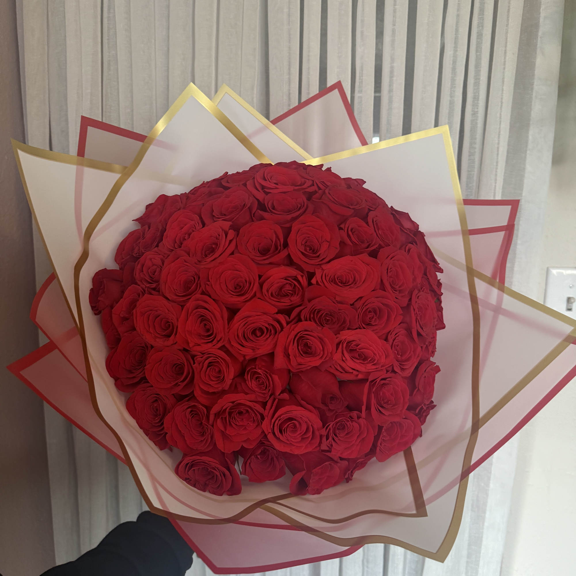 Large bouquet of red roses wrapped in pink and gold paper