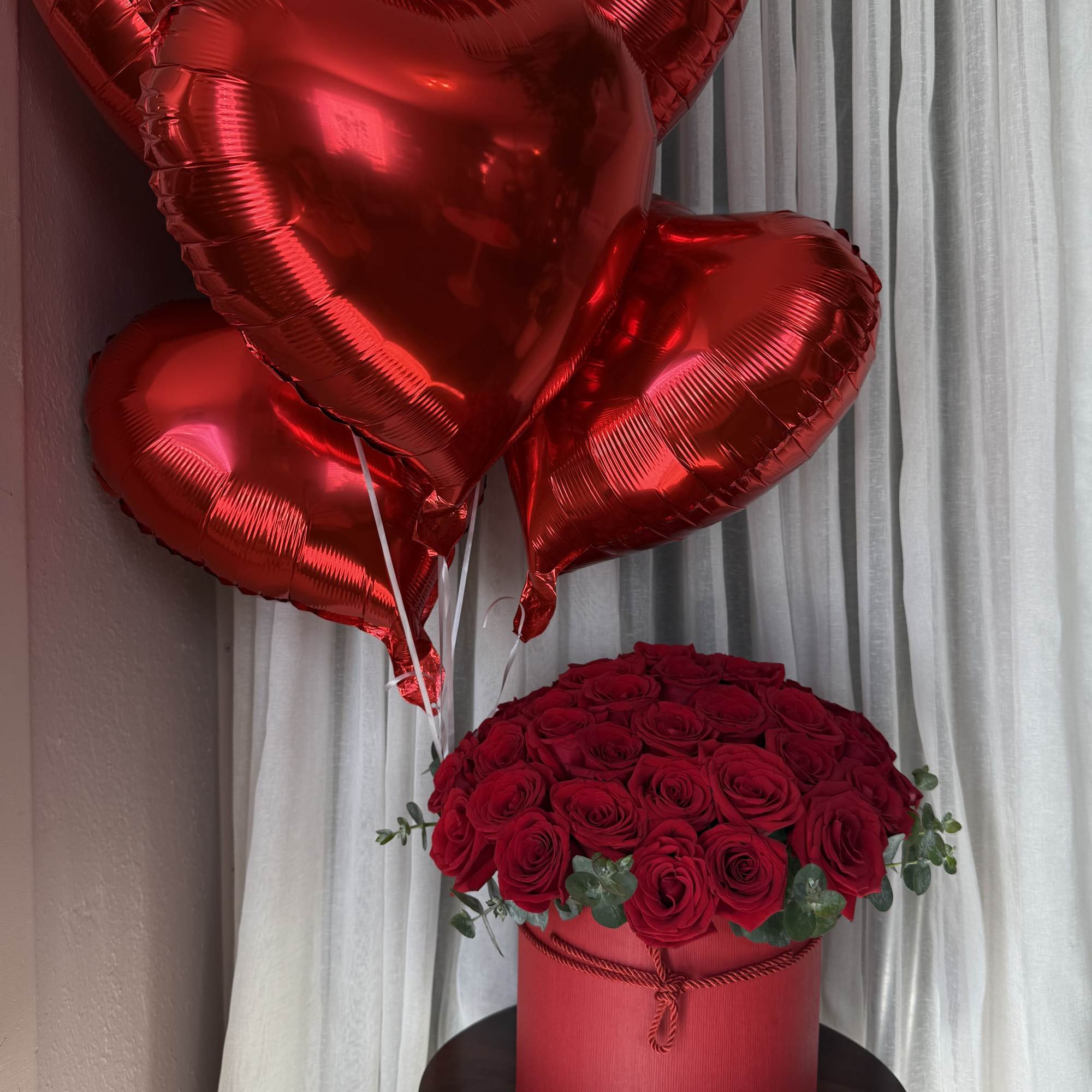 Red rose arrangement with heart-shaped balloons in a red box