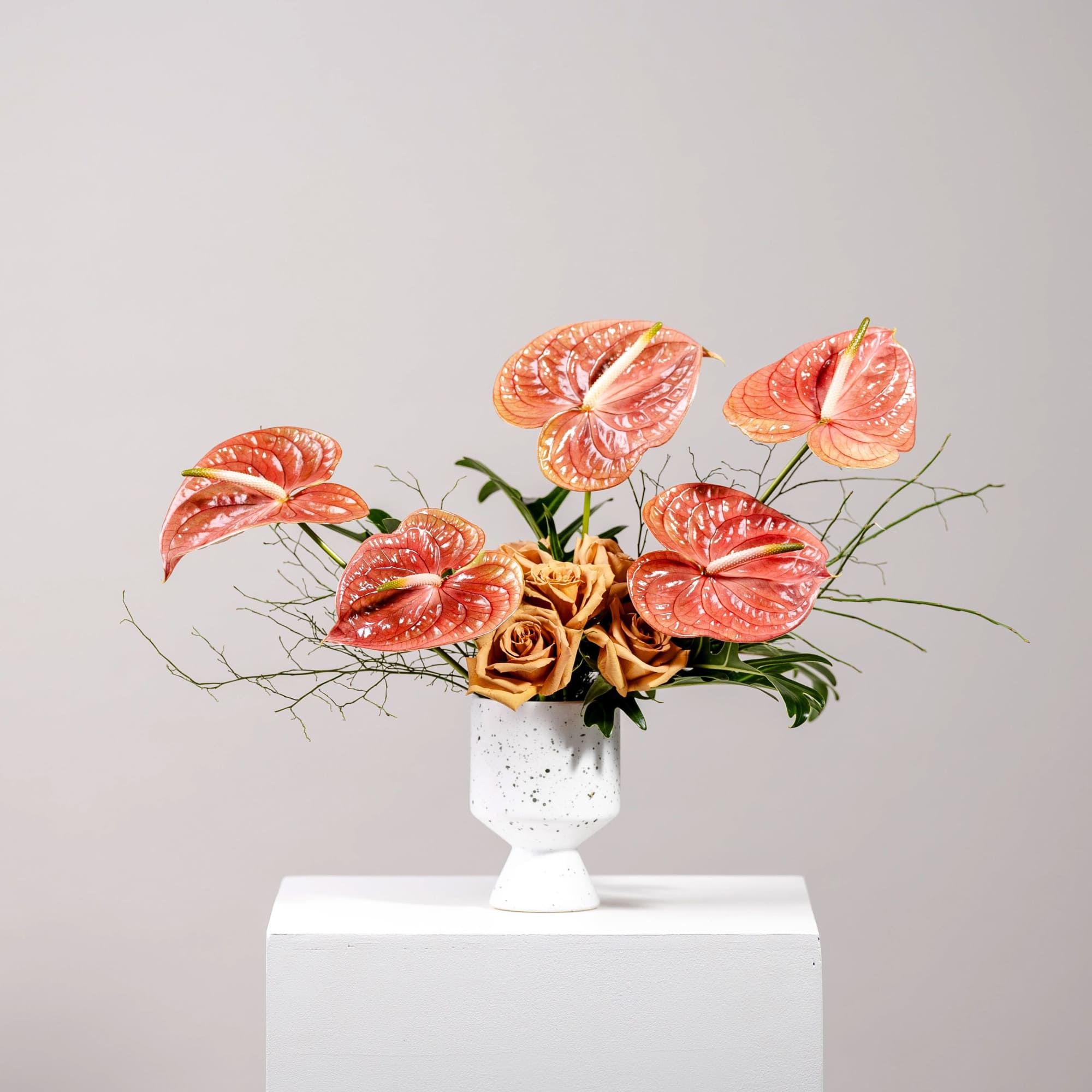 Orange anthuriums and roses arranged in a white vase