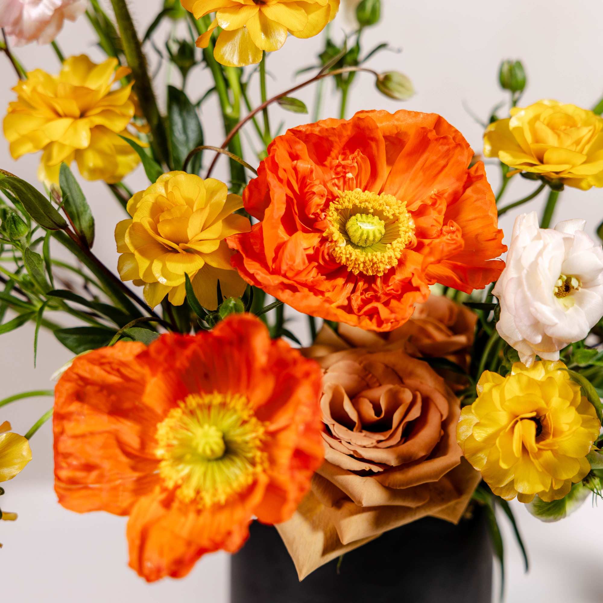 Bouquet of orange and yellow flowers with a tan rose in a black vase