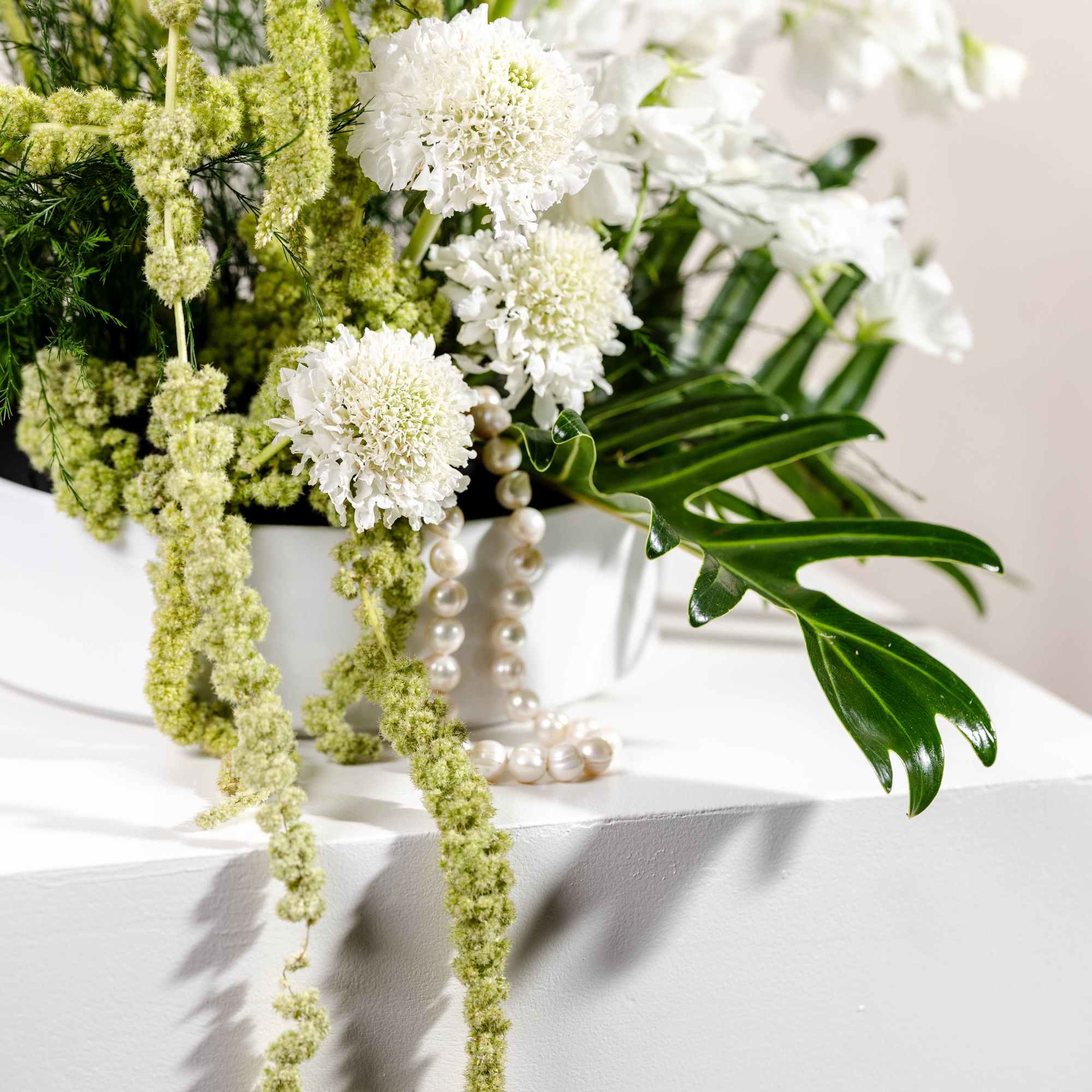 White and green floral arrangement in a white container with trailing blooms