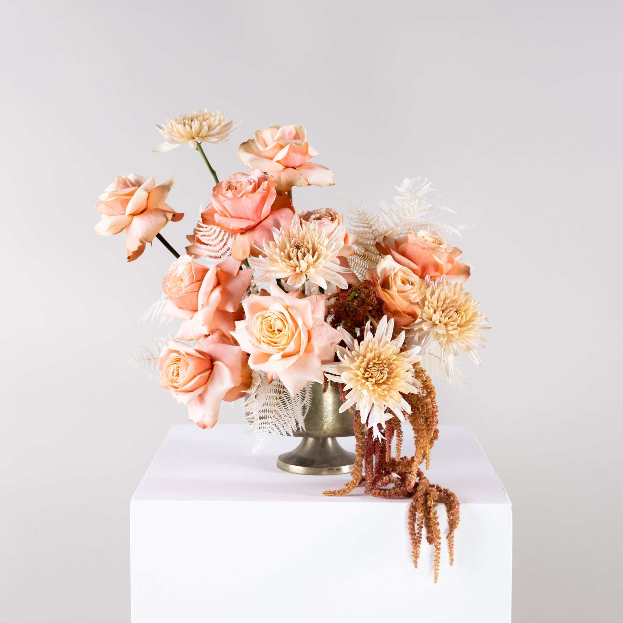 Peach roses and cream blooms arranged in a gold vase