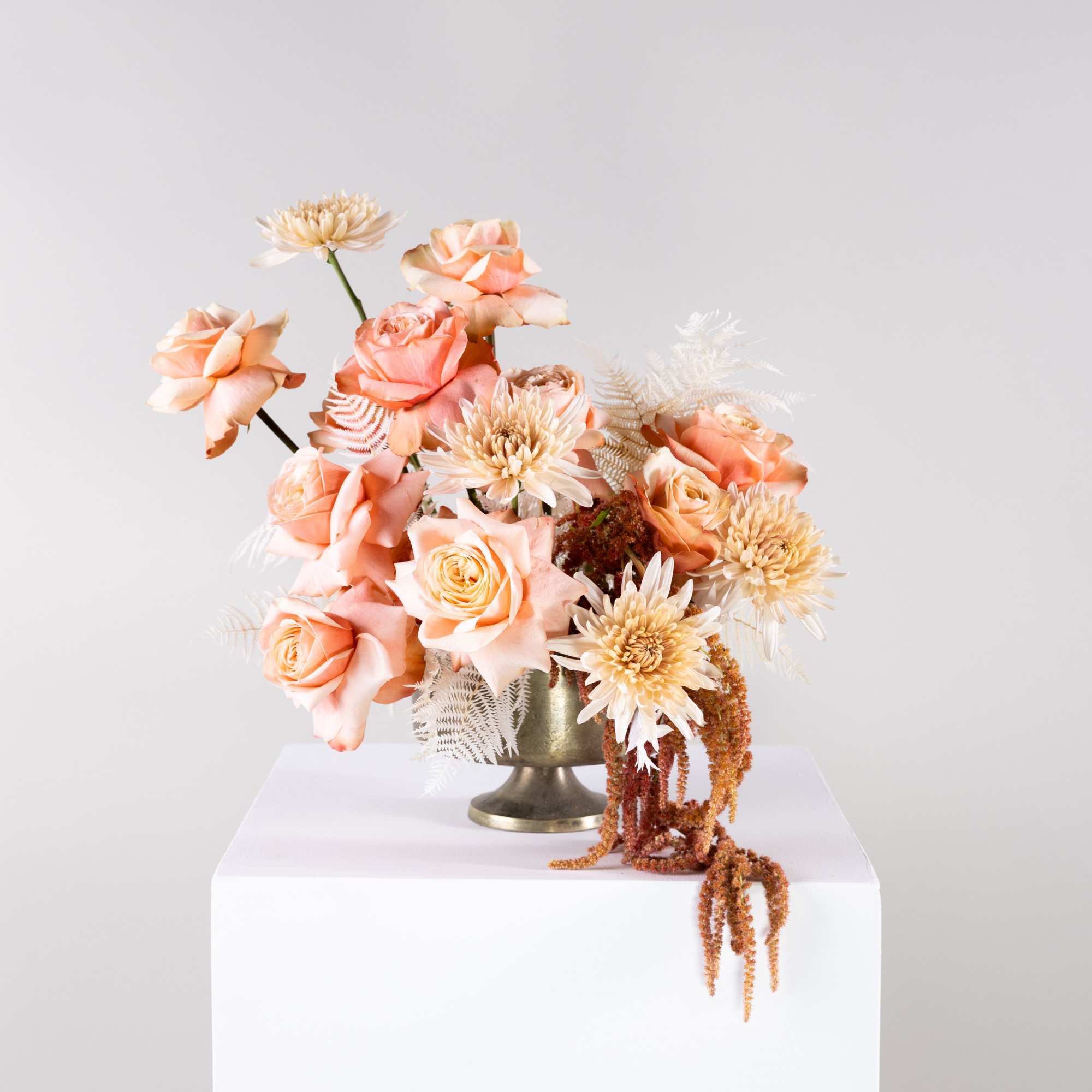 Peach roses and cream flowers arranged in a gold vase
