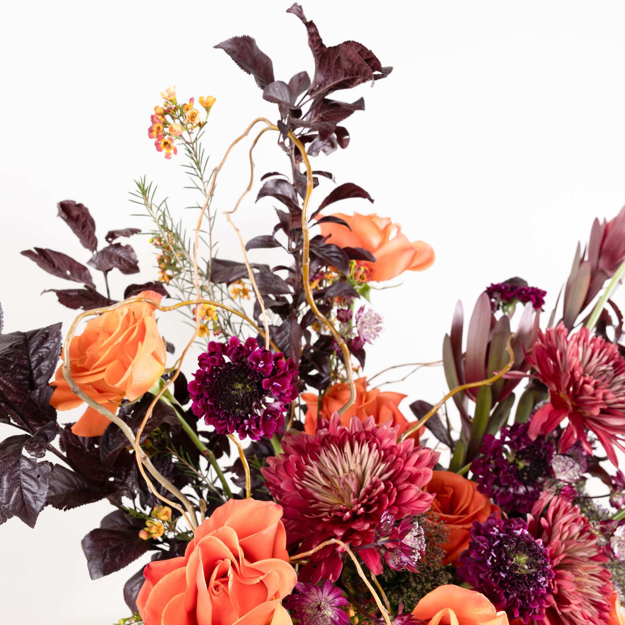 Orange roses and magenta blooms in a dark vase