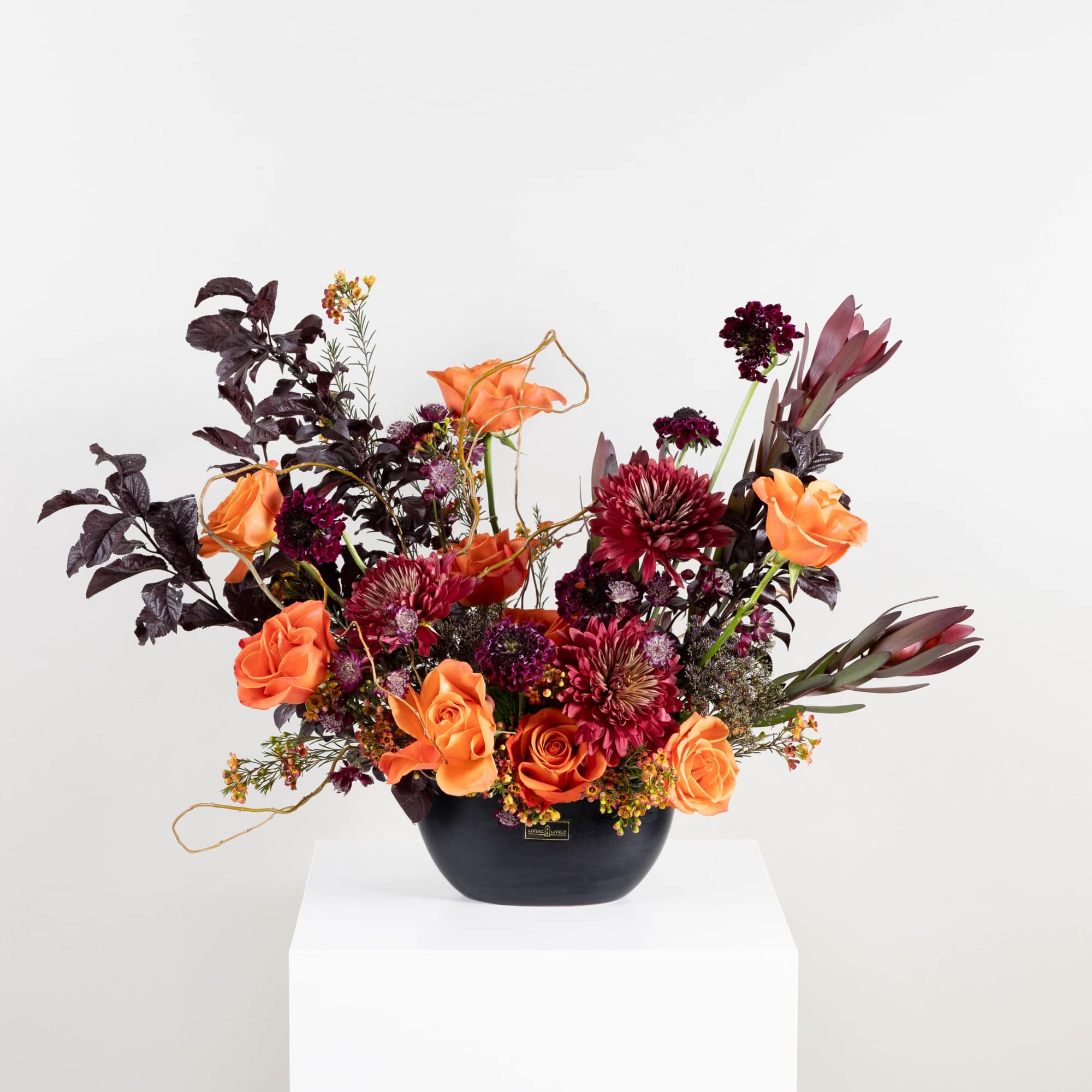 Orange roses and burgundy flowers in a black vase