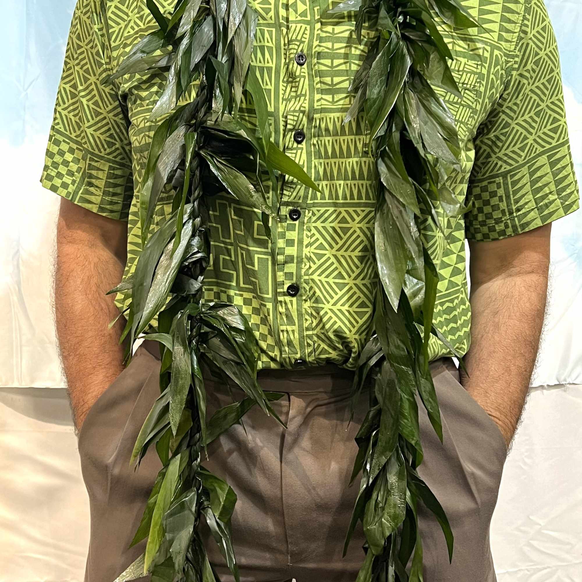 Long leafy green lei draped around a person wearing a patterned green shirt.