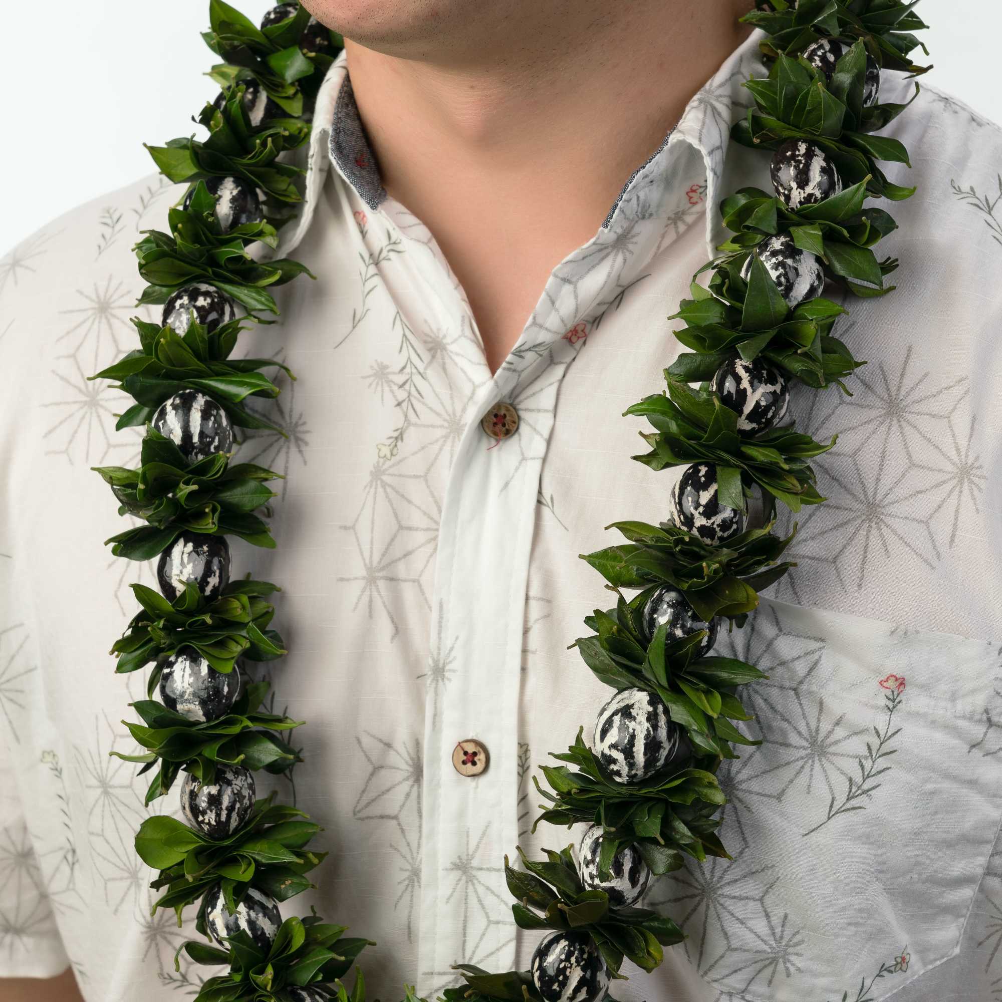 Person wearing a leafy green lei with black and white beads over a light patterned shirt