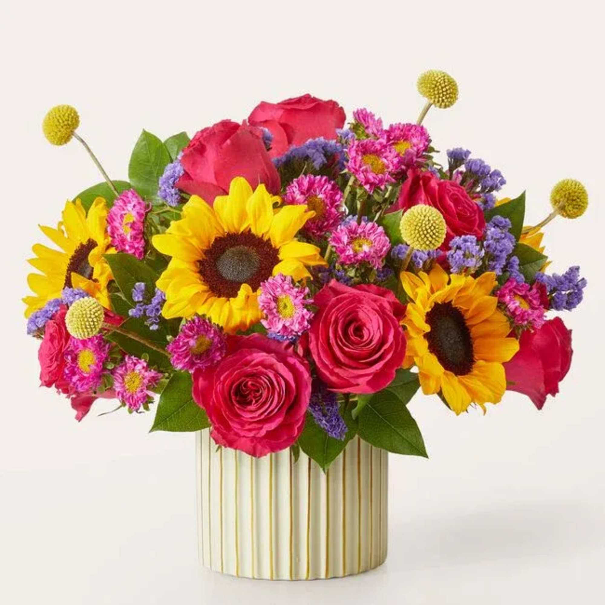 Bright bouquet of sunflowers, pink roses, and purple filler in a striped vase