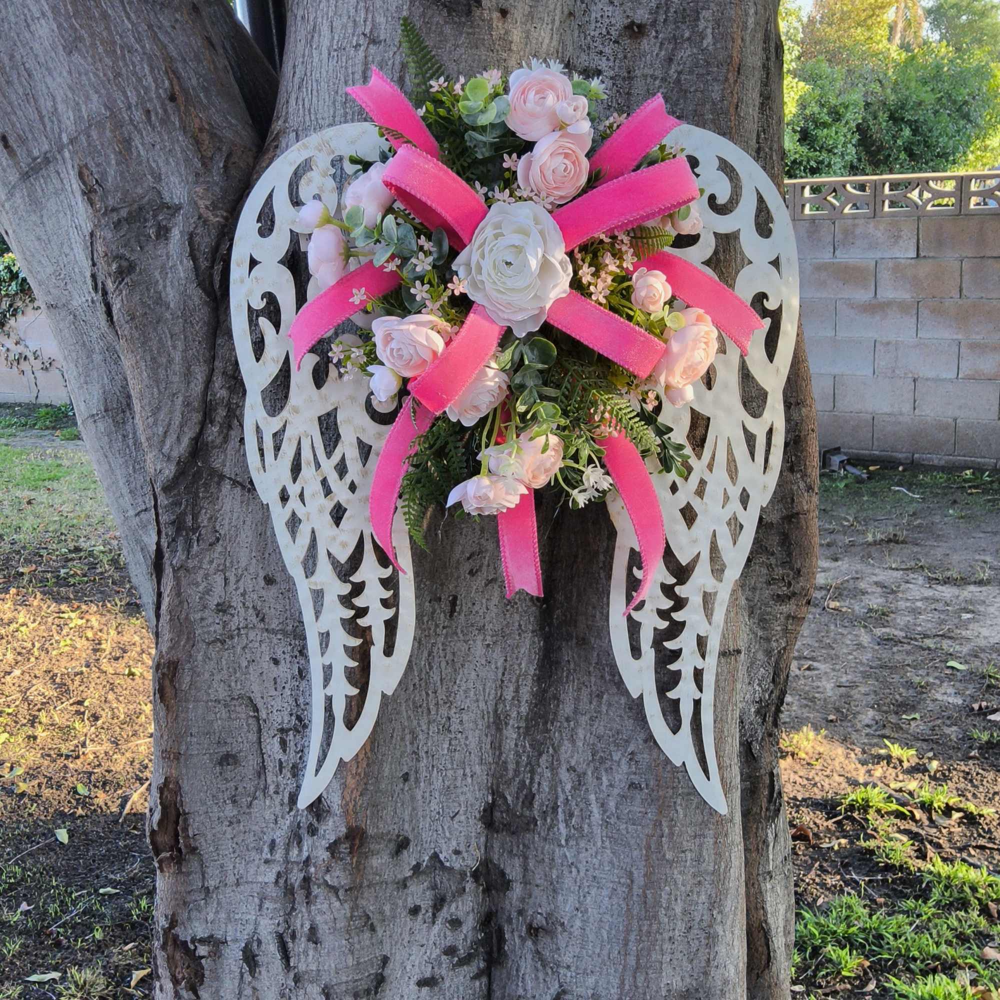 Pink and white floral arrangement on decorative angel wings attached to a tree