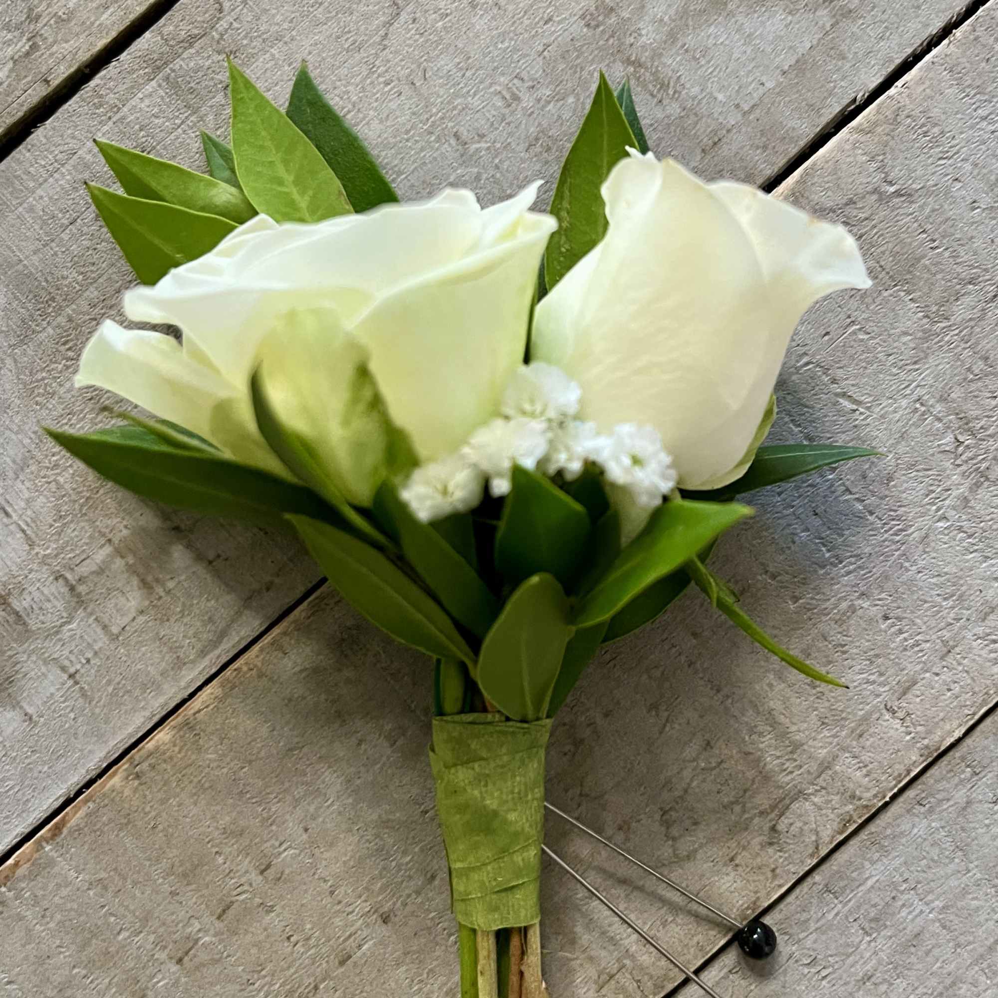 Small white rose boutonniere with green leaves on a wooden surface