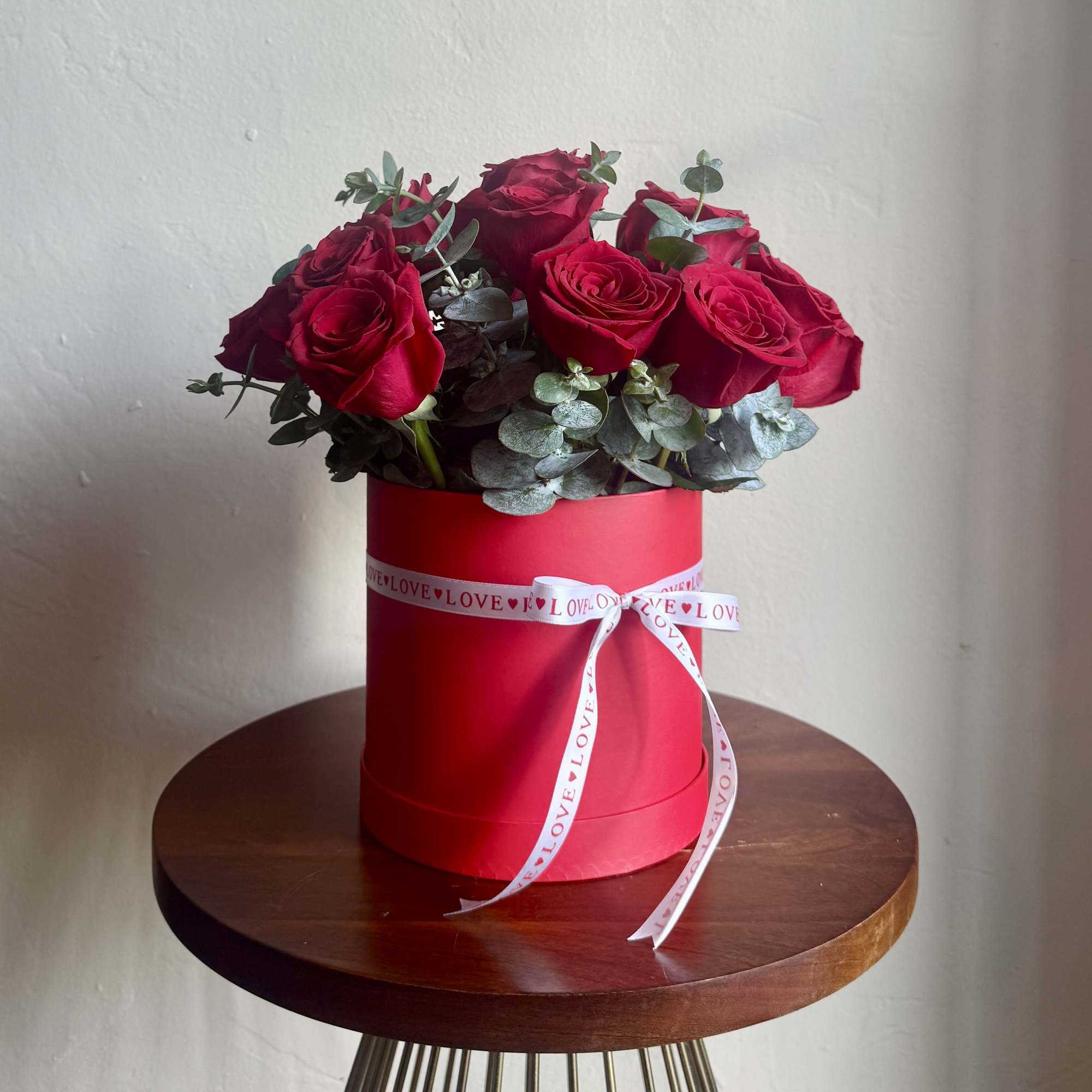 Red roses arranged in a red hat box with a white ribbon