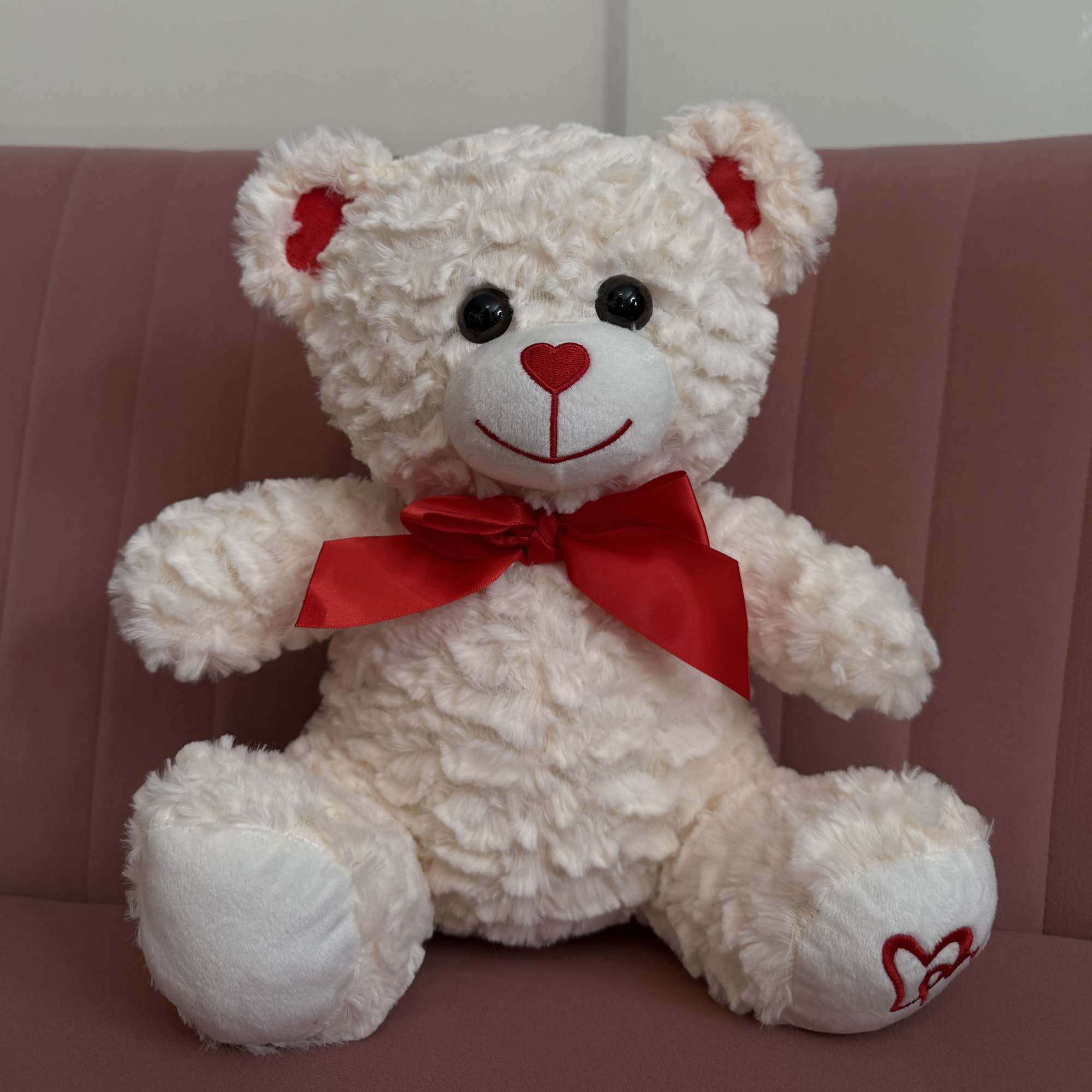White teddy bear with a red bow sitting on a pink chair