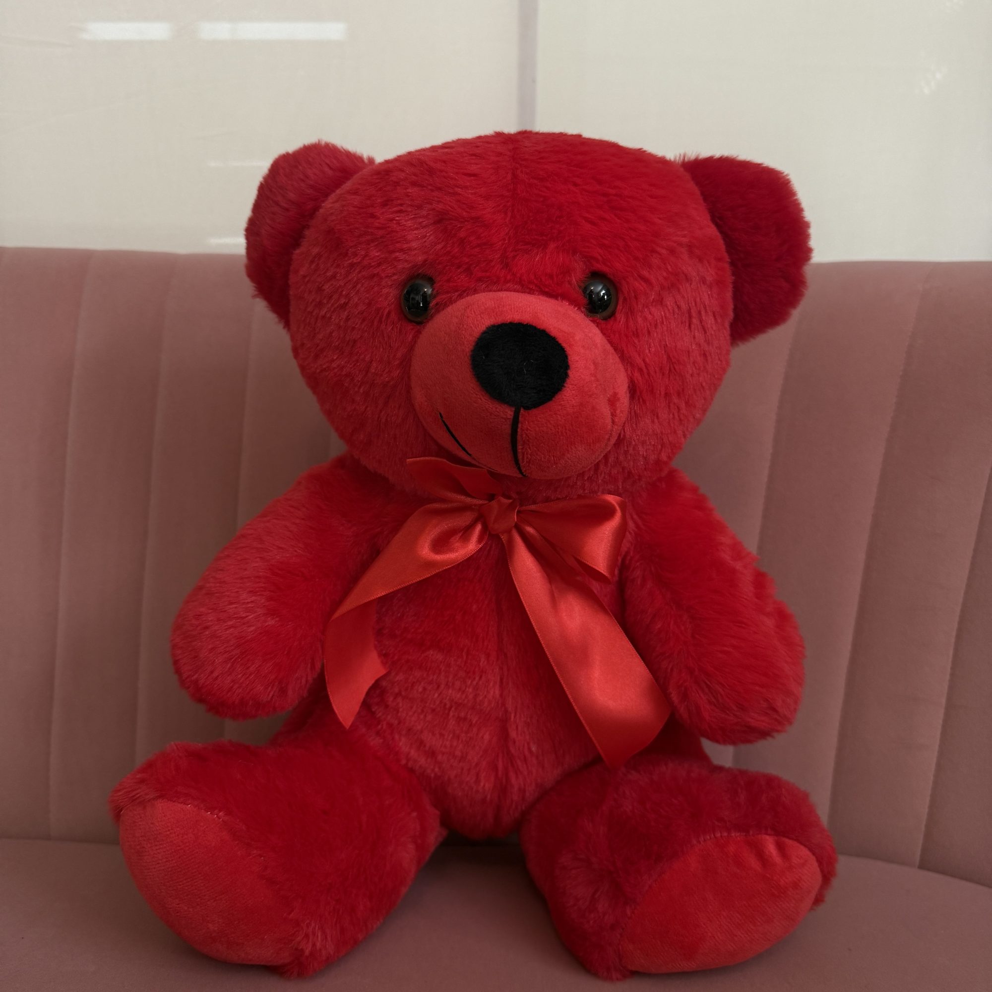 Red teddy bear with a satin bow sitting on a chair