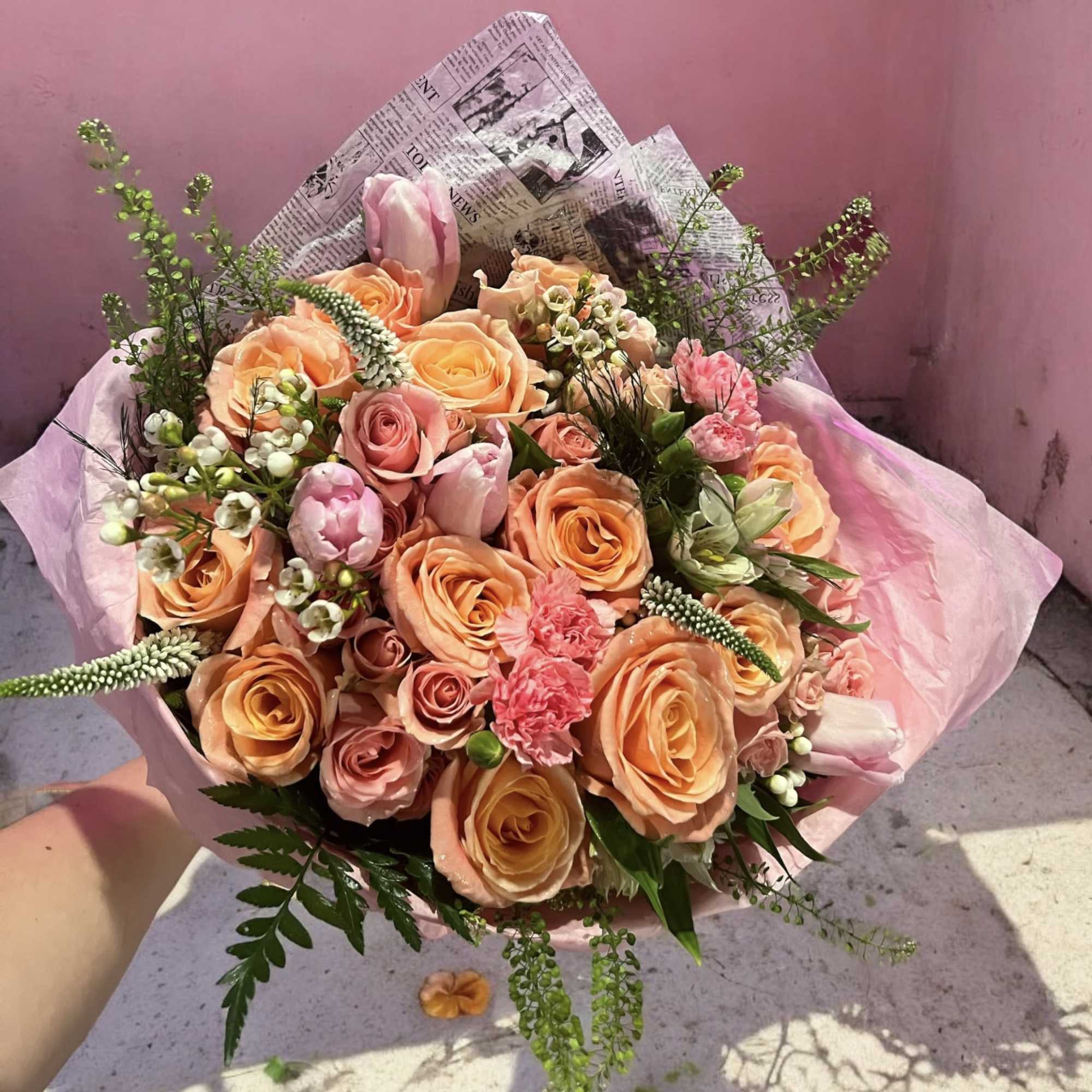 Bouquet of peach and pink roses with tulips and greenery wrapped in pink paper