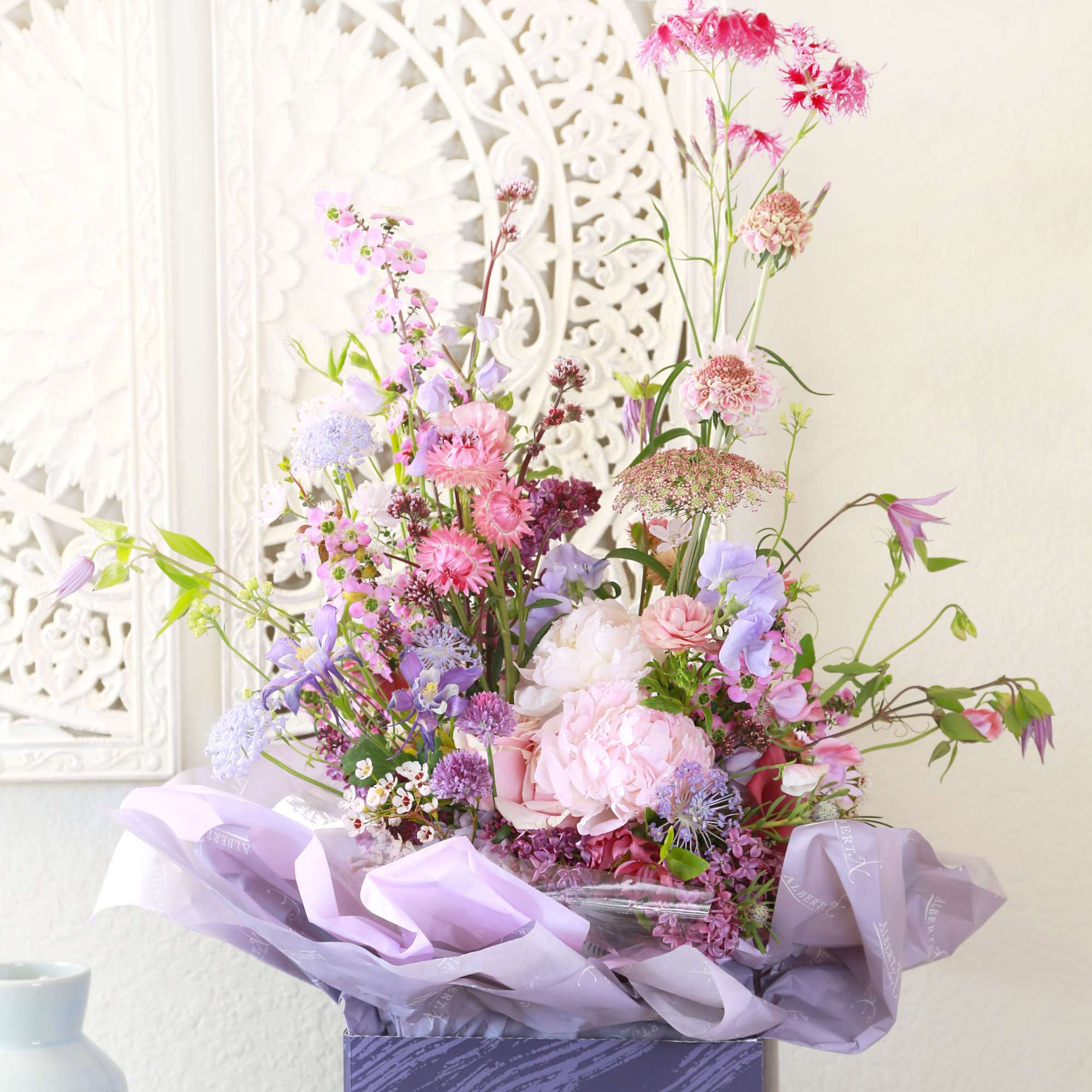 Lavender and pink garden-style flower arrangement in a purple box with tissue wrap.