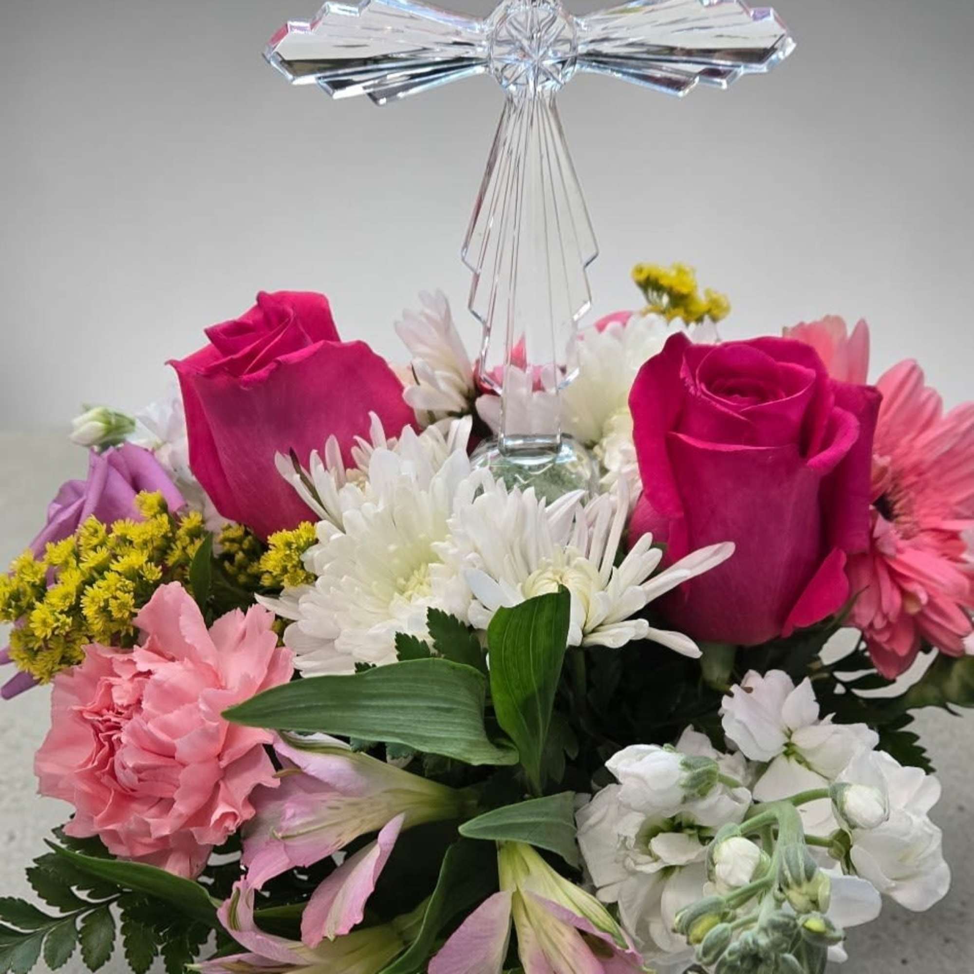 A graceful arrangement featuring a crystal cross surrounded by pink roses, white