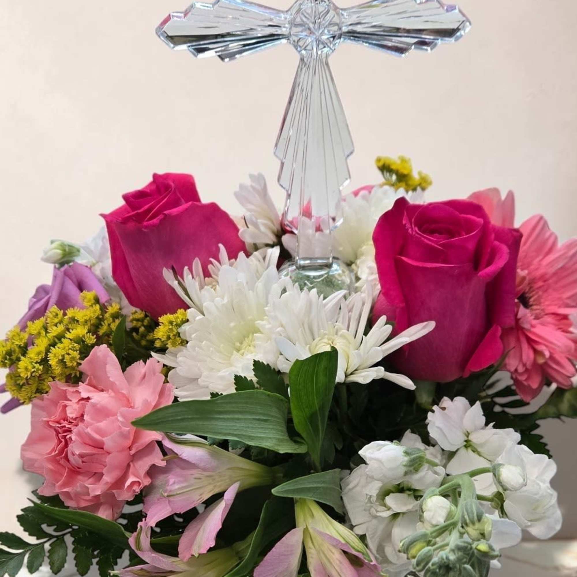 A graceful arrangement featuring a crystal cross surrounded by pink roses, white