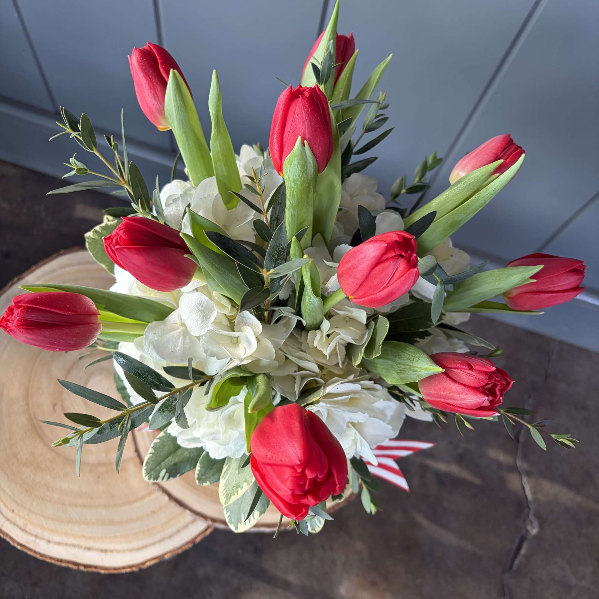 Top view of a bouquet of red tulips and white hydrangeas arranged on a wooden slice base.