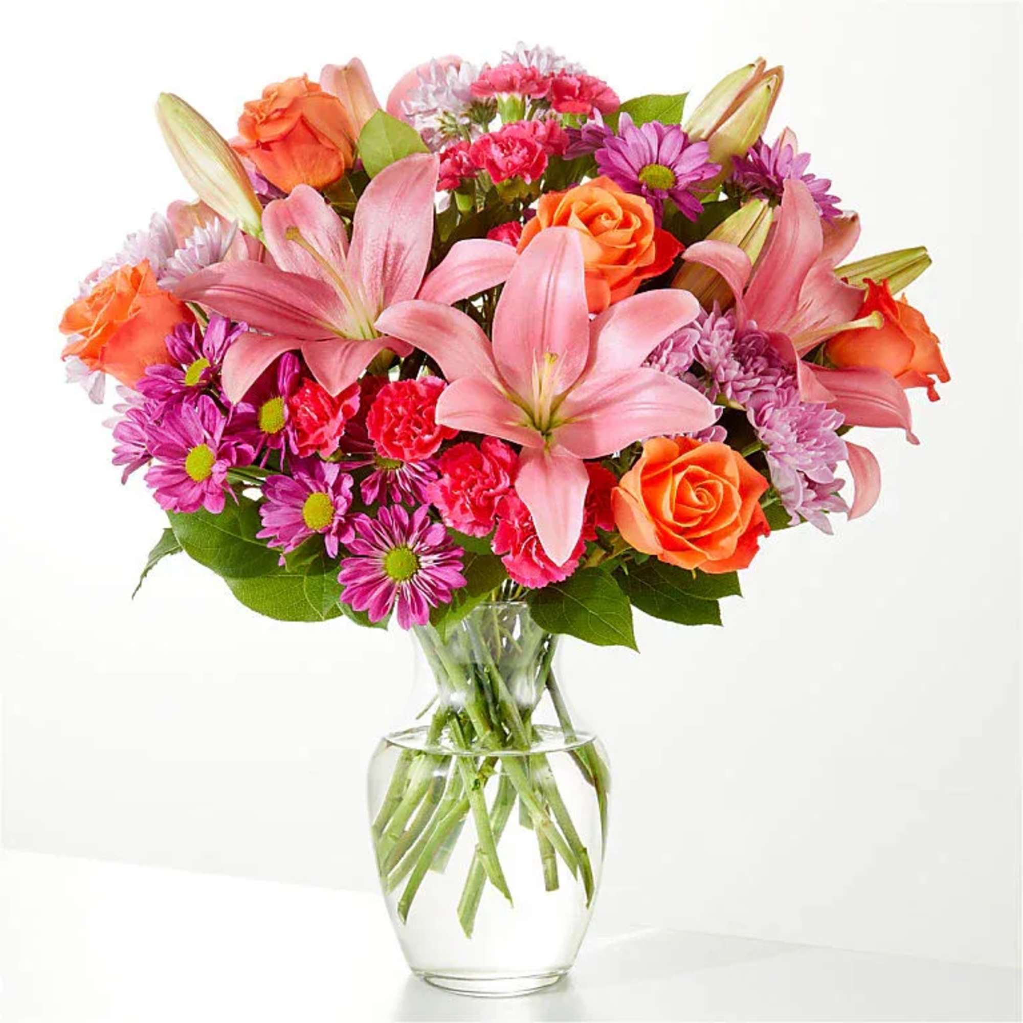 Pink lilies, orange roses, and purple daisies in a clear glass vase