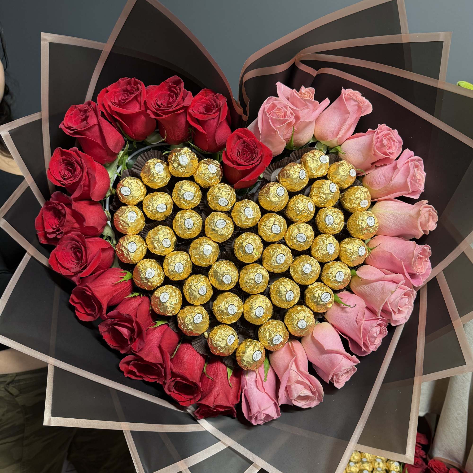 Heart-shaped arrangement of gold-wrapped chocolates edged with red and pink roses in dark wrapping paper