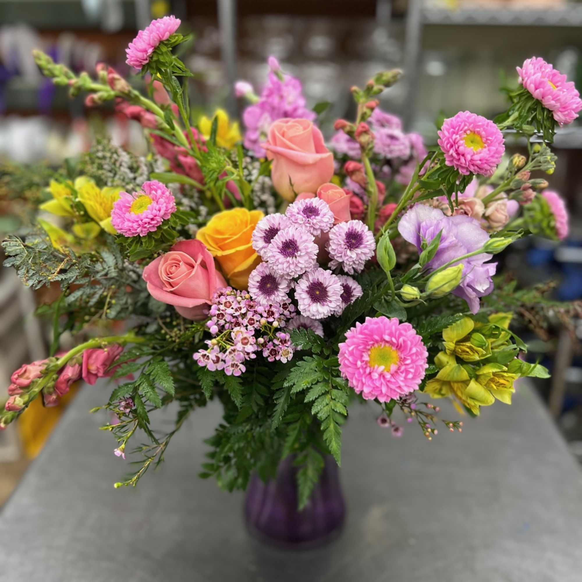 Mixed bouquet of pink roses and colorful daisies in a purple vase