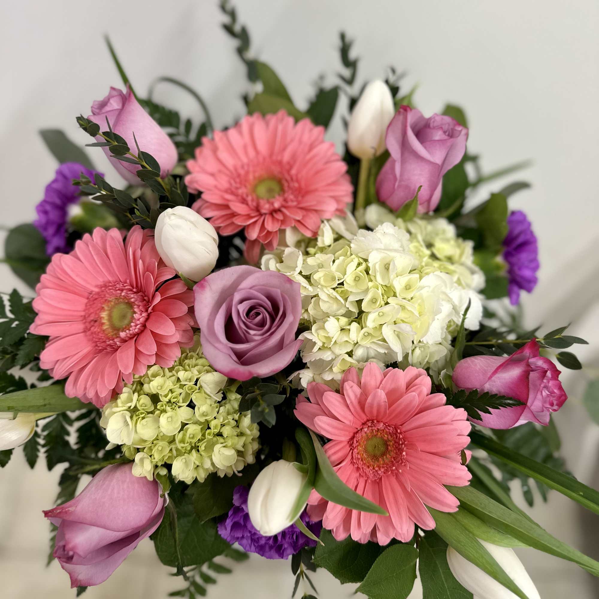 Pink gerbera daisies, lavender roses, hydrangea, and white tulips in a mixed bouquet.