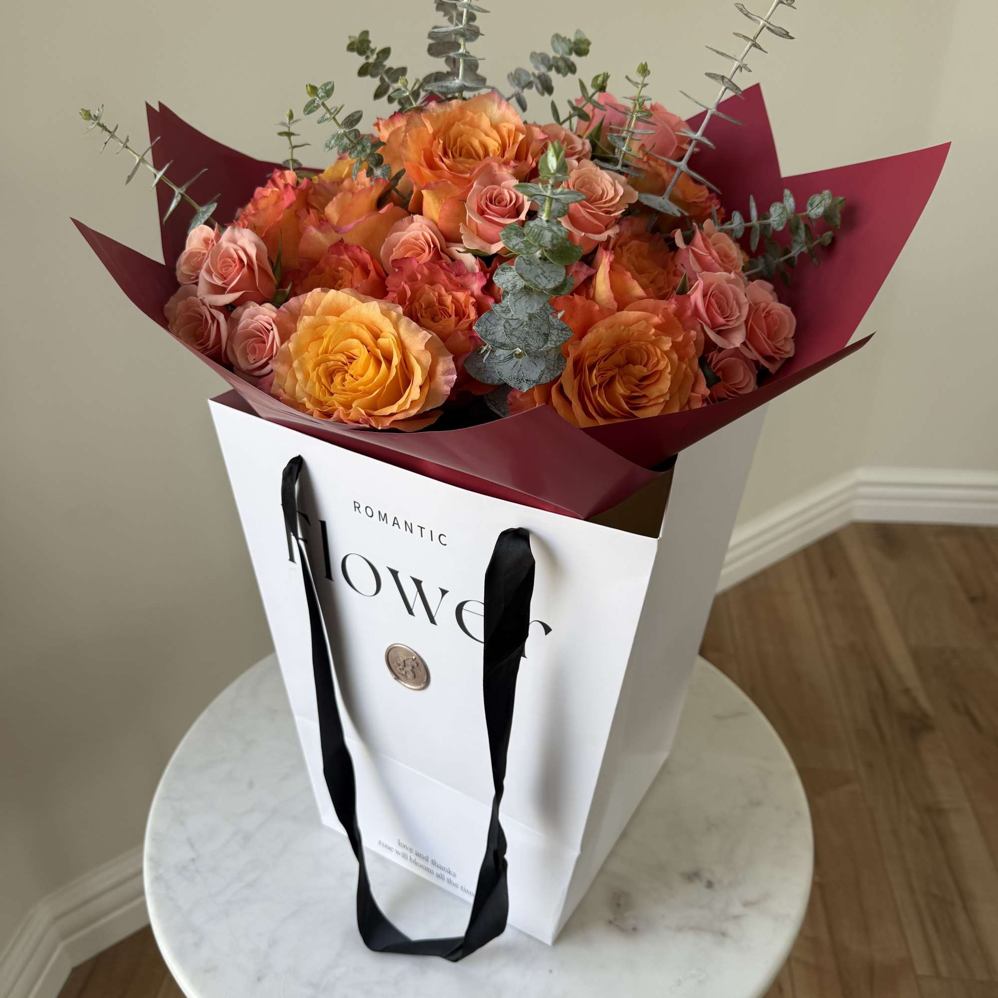Orange and pink roses in a white gift bag with burgundy wrapping