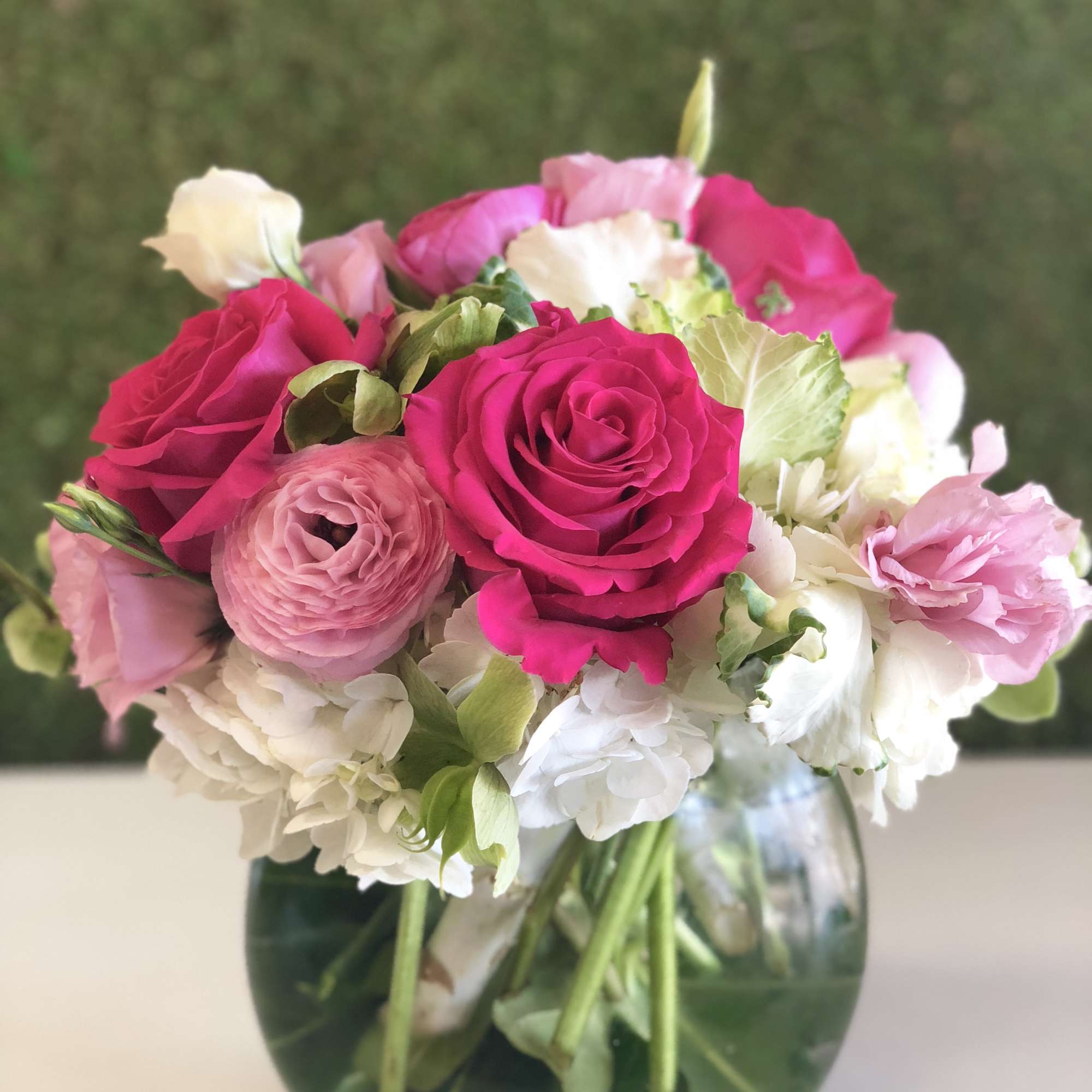 Pink and white bouquet of roses, ranunculus, and hydrangeas in a glass vase