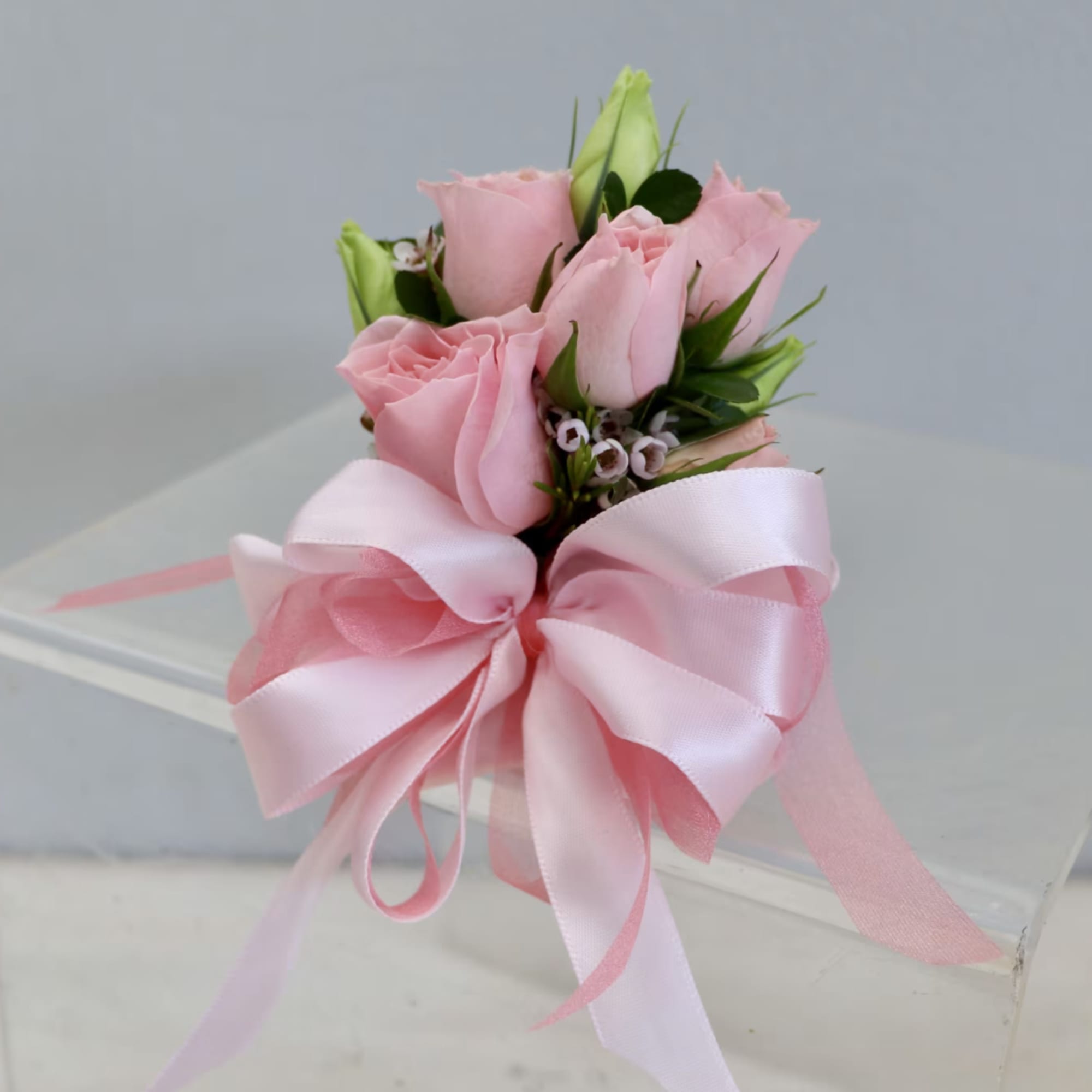 Pink rose corsage with a large pink ribbon bow on a clear acrylic stand