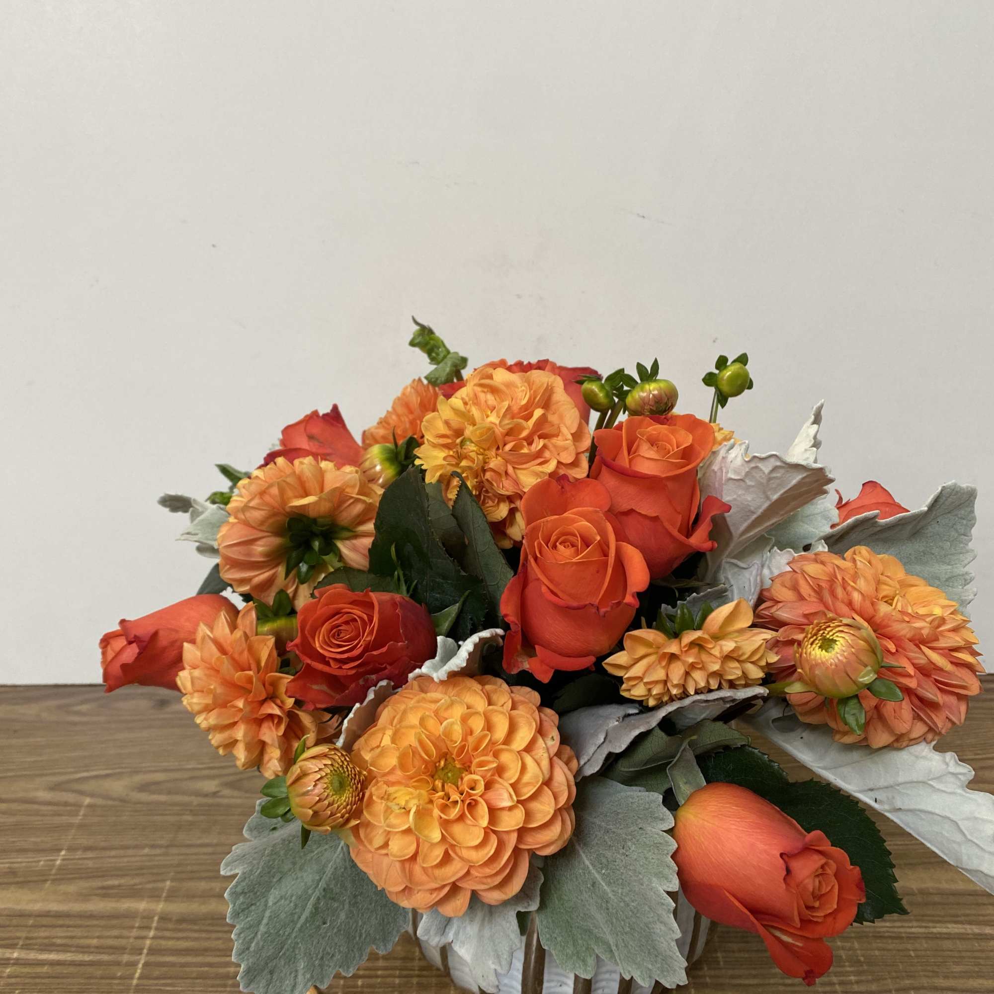 In a glass vase combinations of orange dollar and orange roses