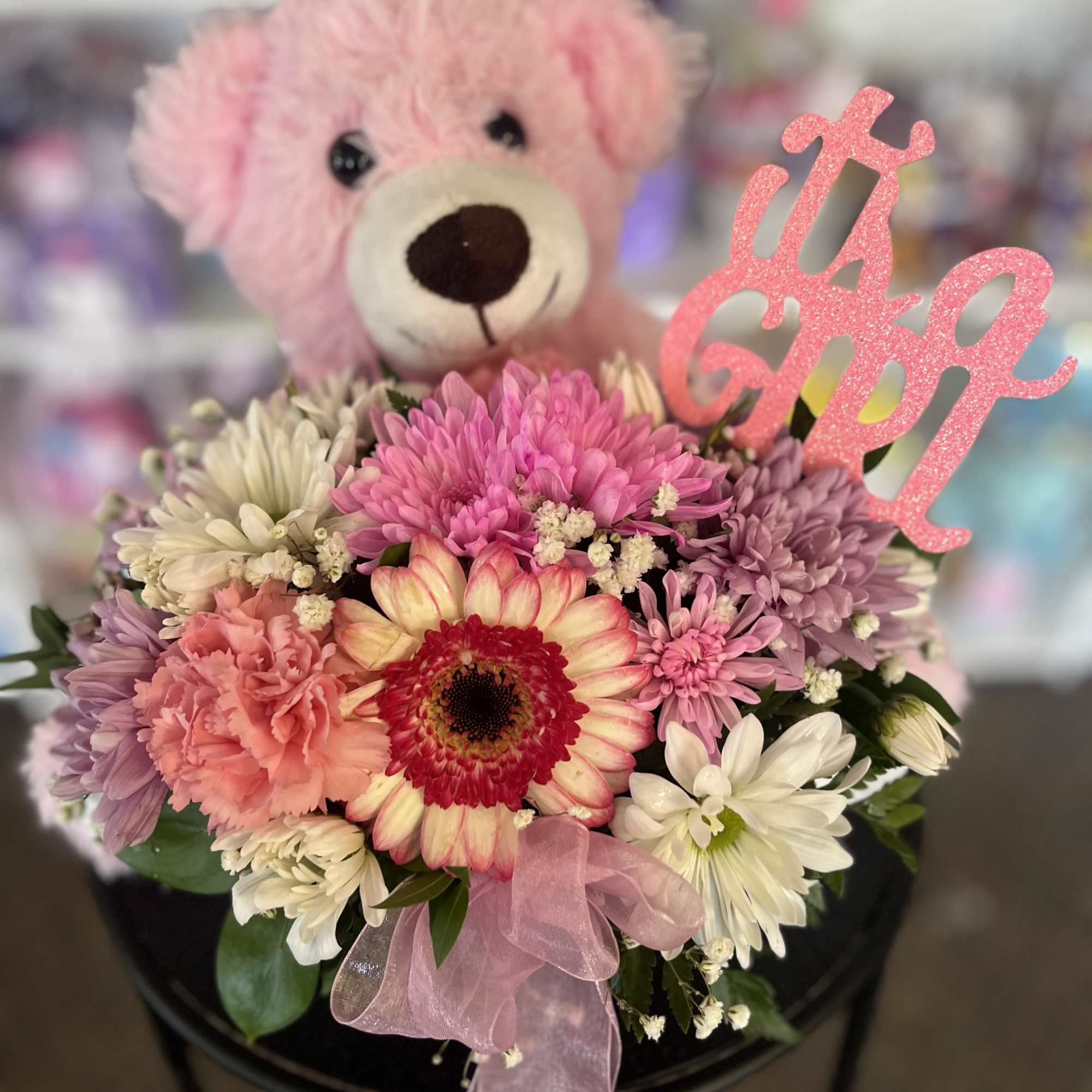 Pink teddy bear behind a pastel flower bouquet with a glittery topper