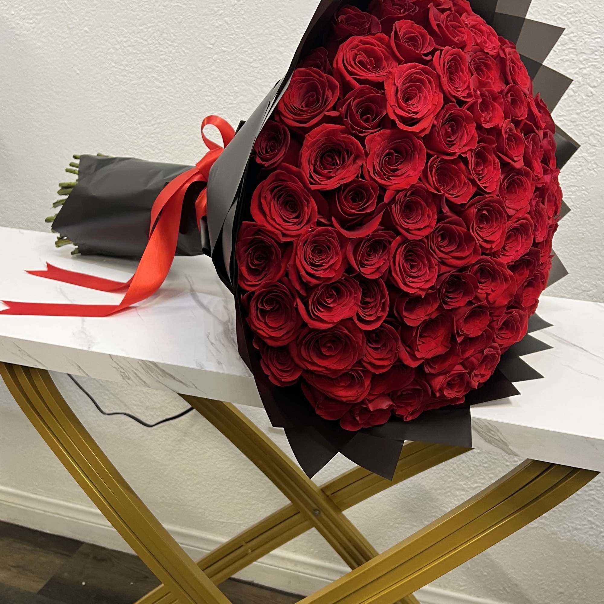 Large bouquet of red roses wrapped in black paper with a red ribbon