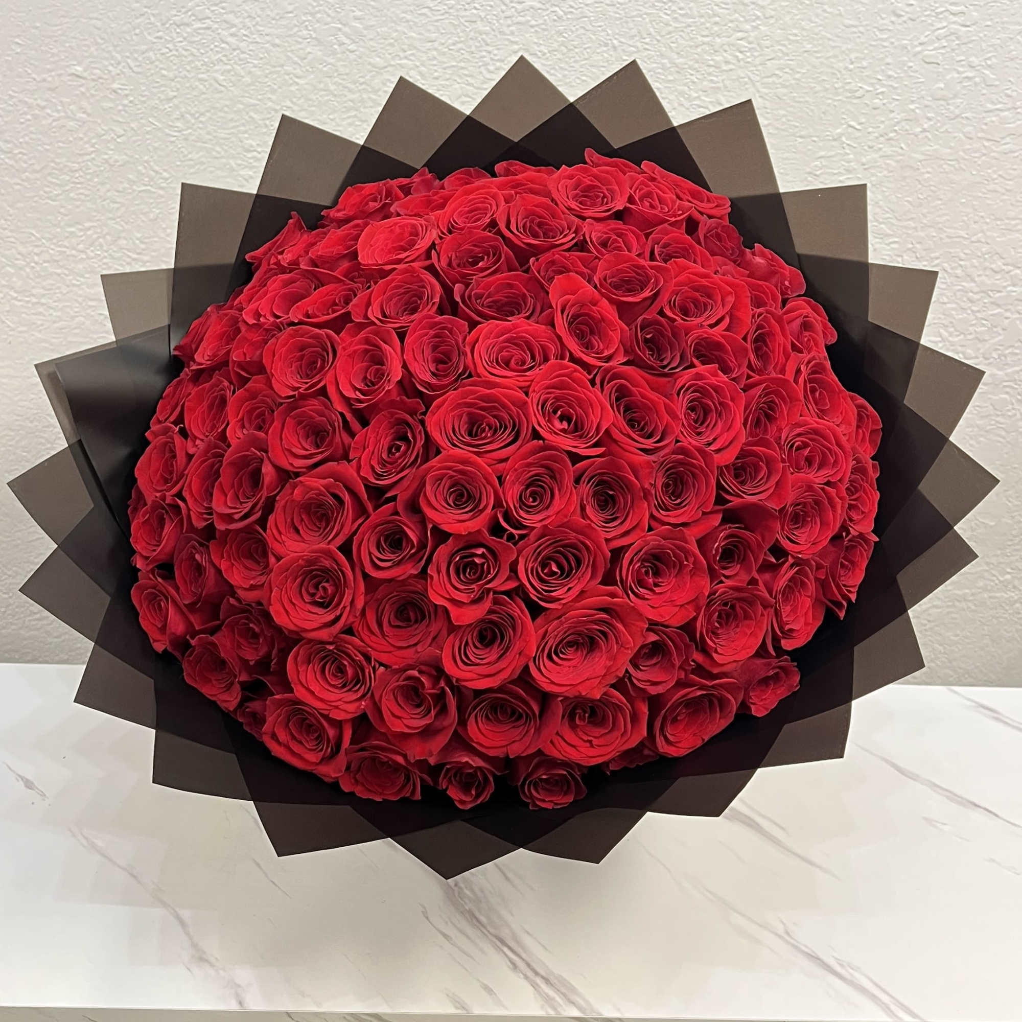 Large round bouquet of red roses wrapped in dark paper