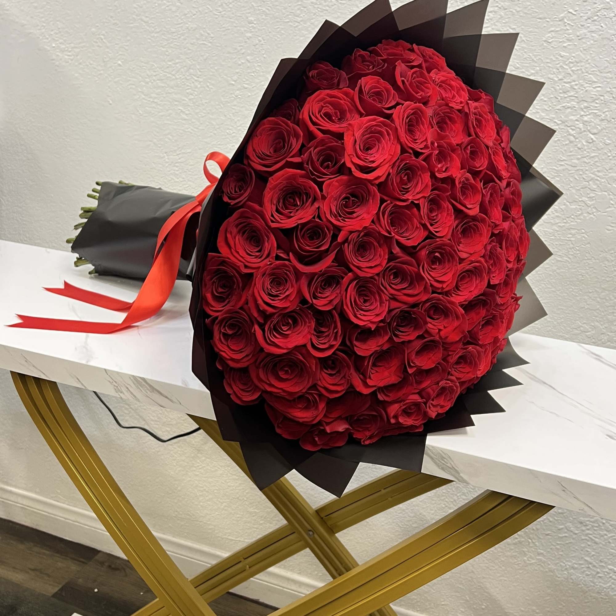 Large bouquet of red roses wrapped in black paper with a red ribbon