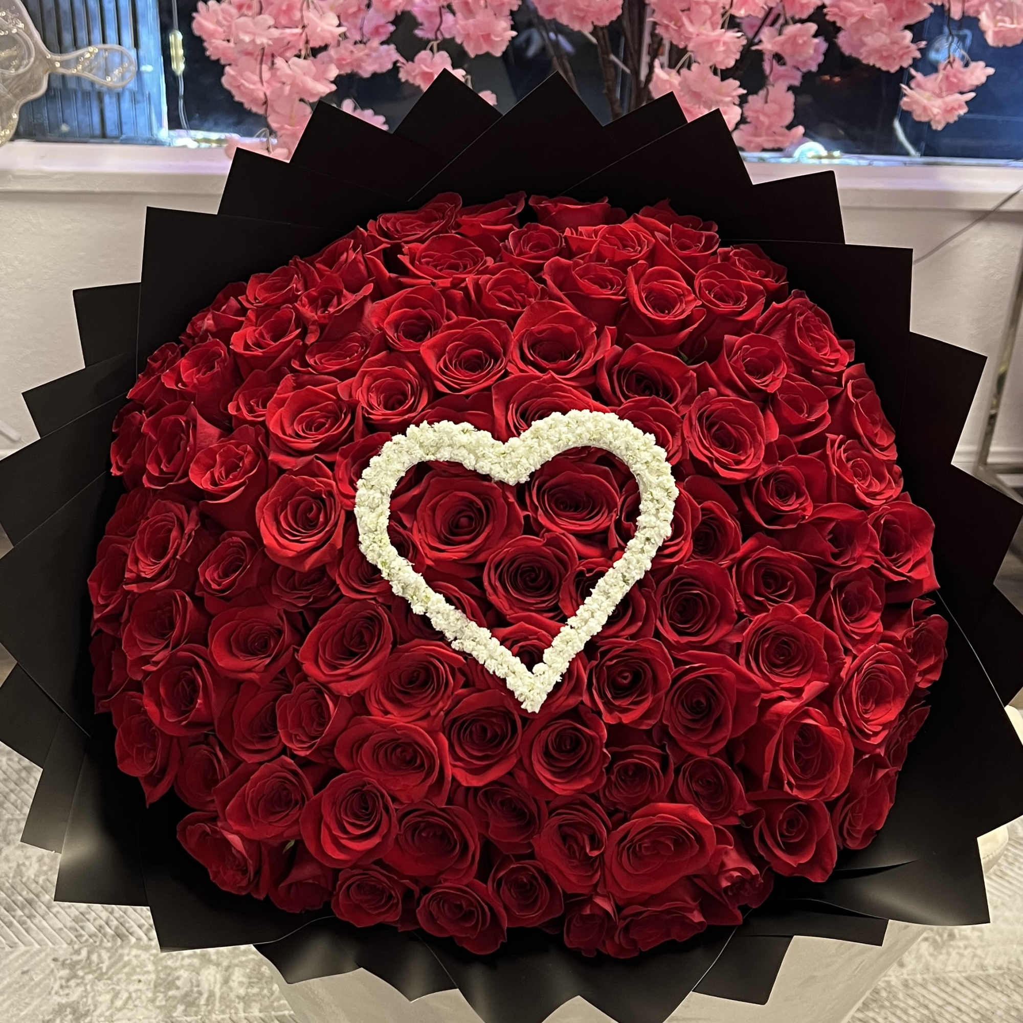 Large bouquet of red roses with a white heart accent in black wrap
