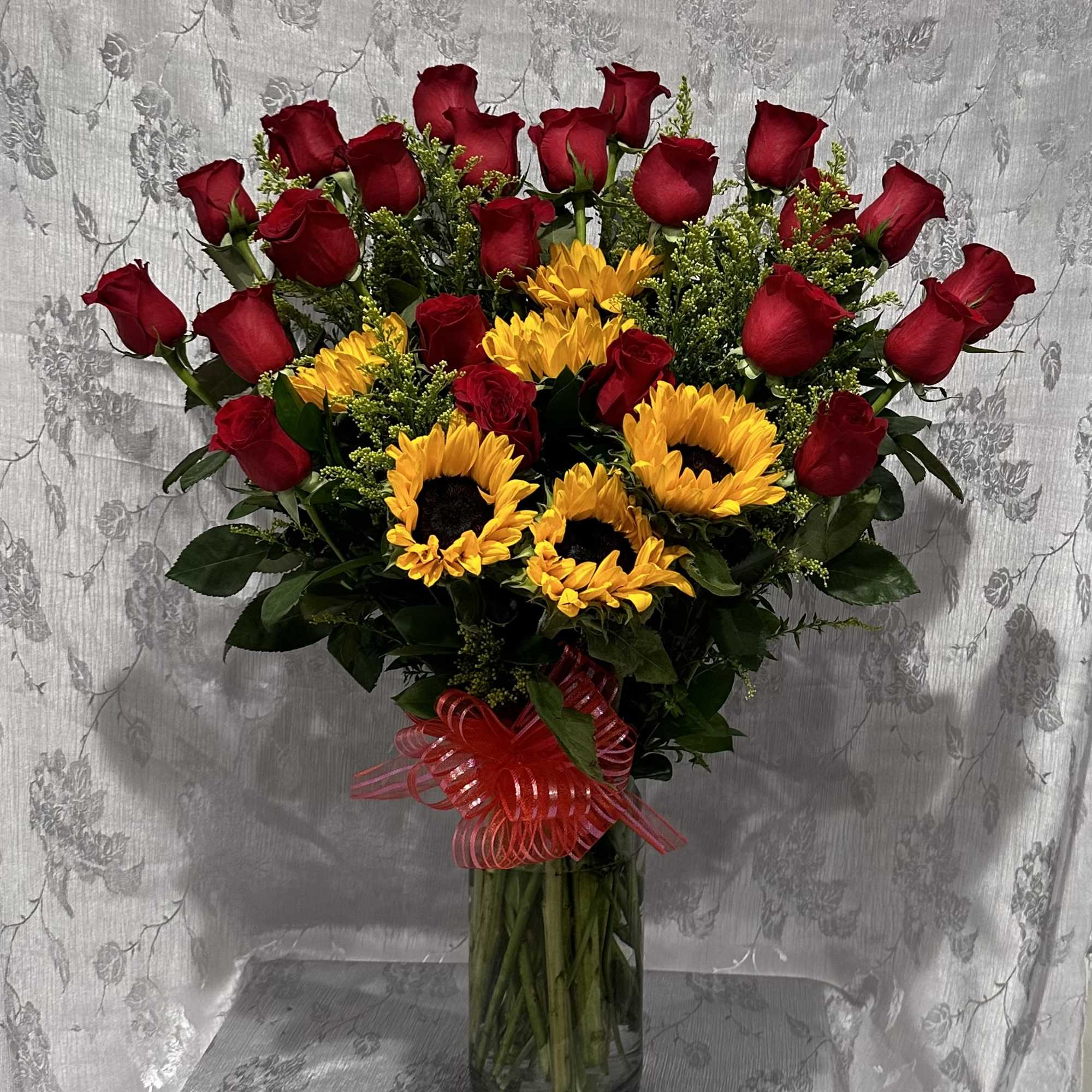 Bouquet of red roses and yellow sunflowers in a glass vase with a red ribbon