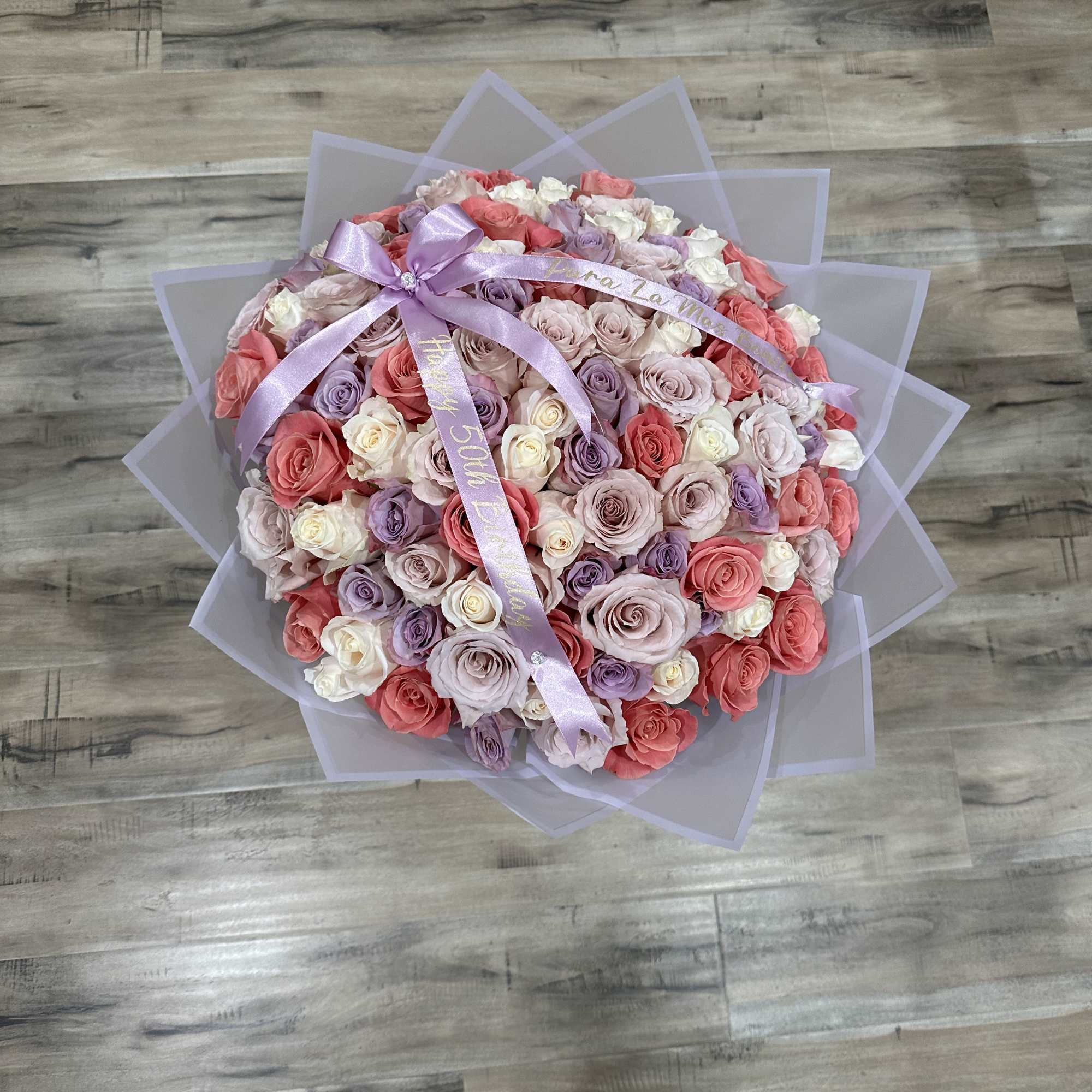 Large bouquet of pastel roses wrapped in lavender paper with a ribbon