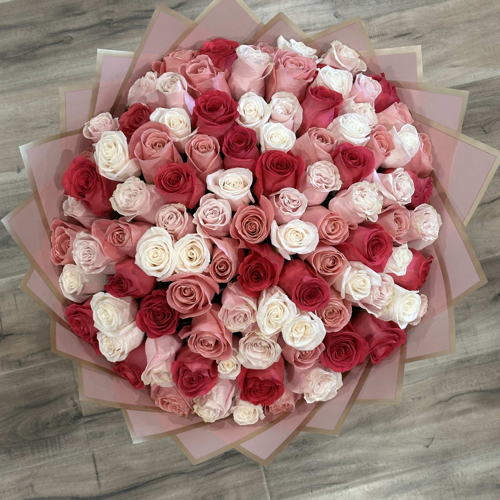 Large bouquet of pink, red, and white roses wrapped in pink paper