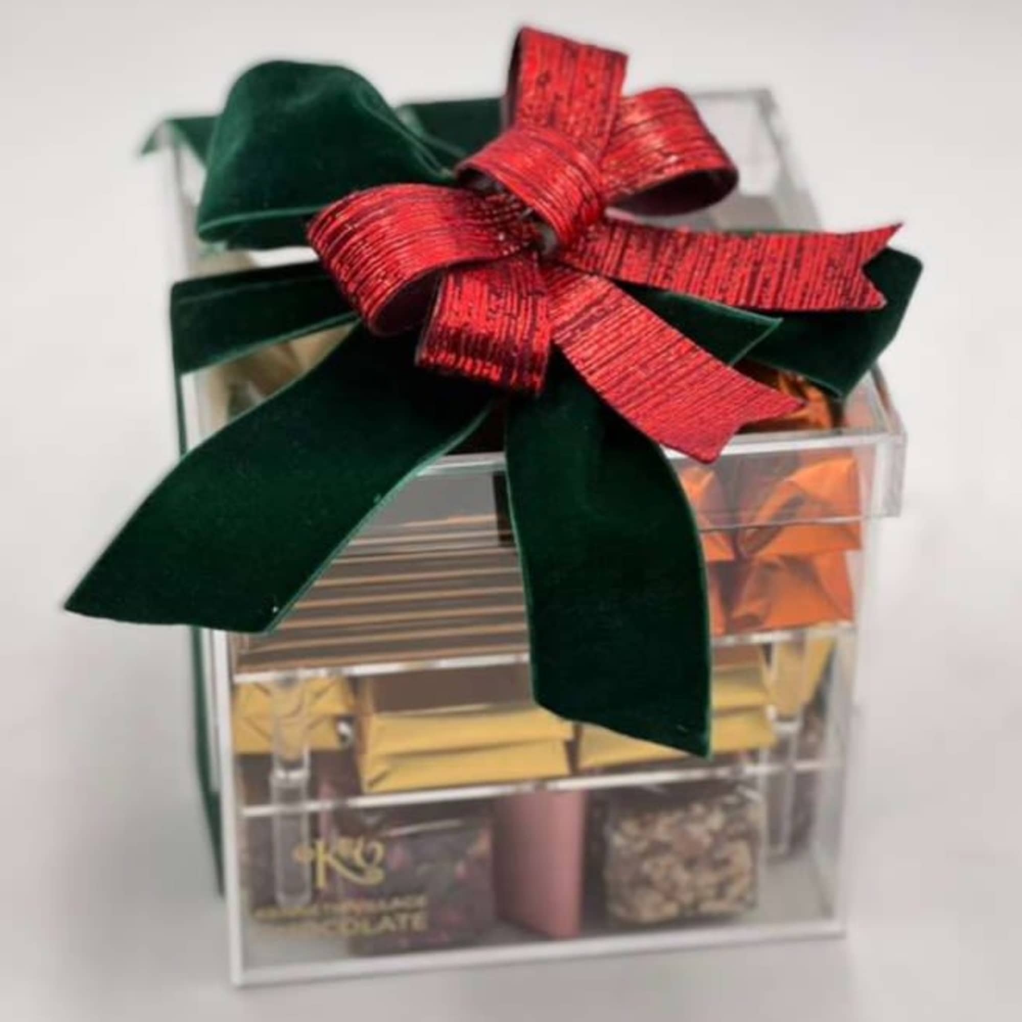 Clear gift box tied with a red and green ribbon, filled with assorted chocolates
