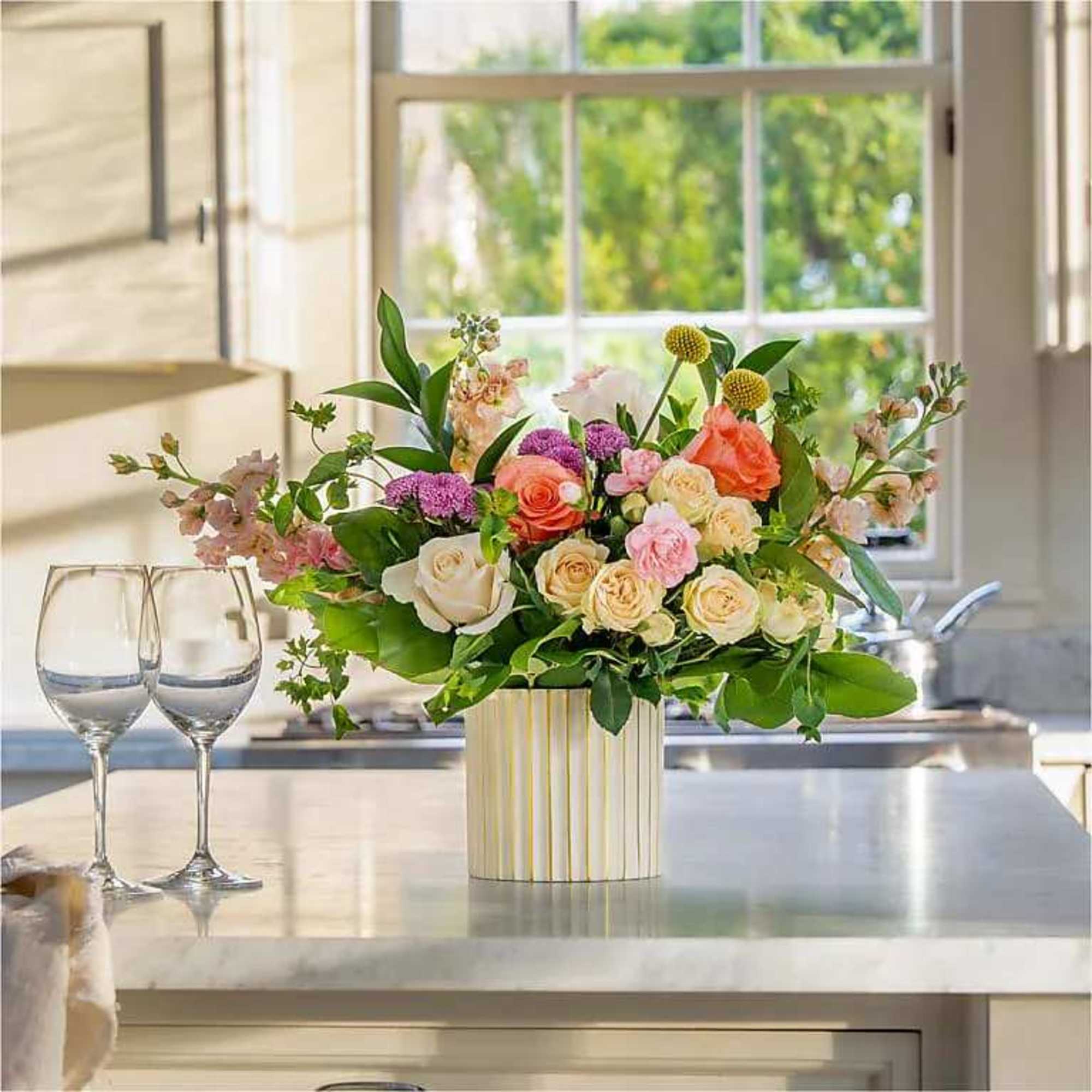 Mixed bouquet of pastel roses and purple blooms in a striped vase