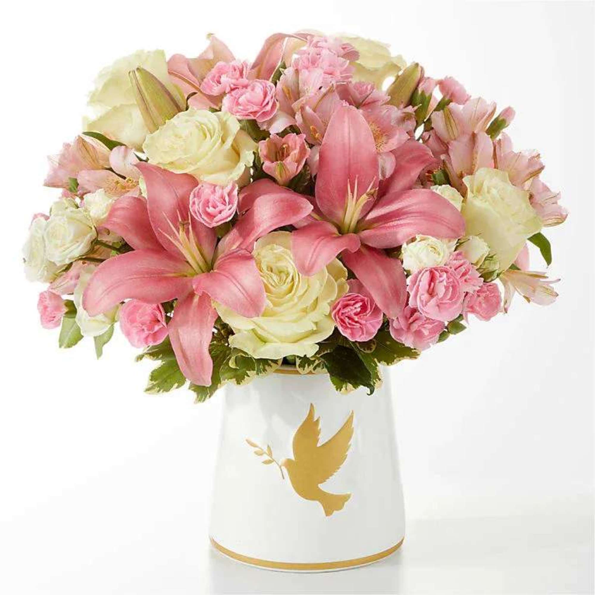 Pink lilies and cream roses arranged in a white vase with a gold dove