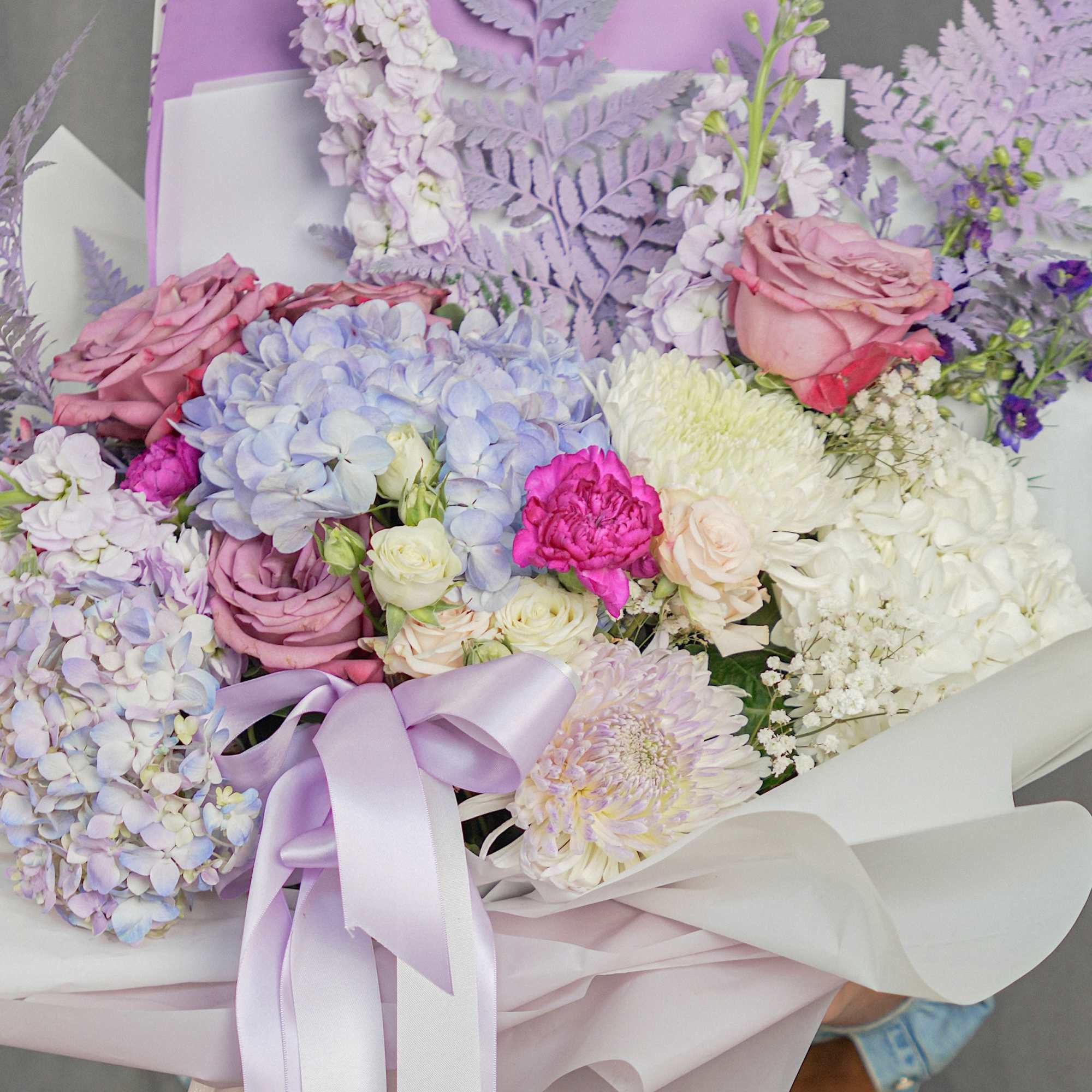 Pastel bouquet with hydrangeas, roses, and chrysanthemums wrapped in lavender paper